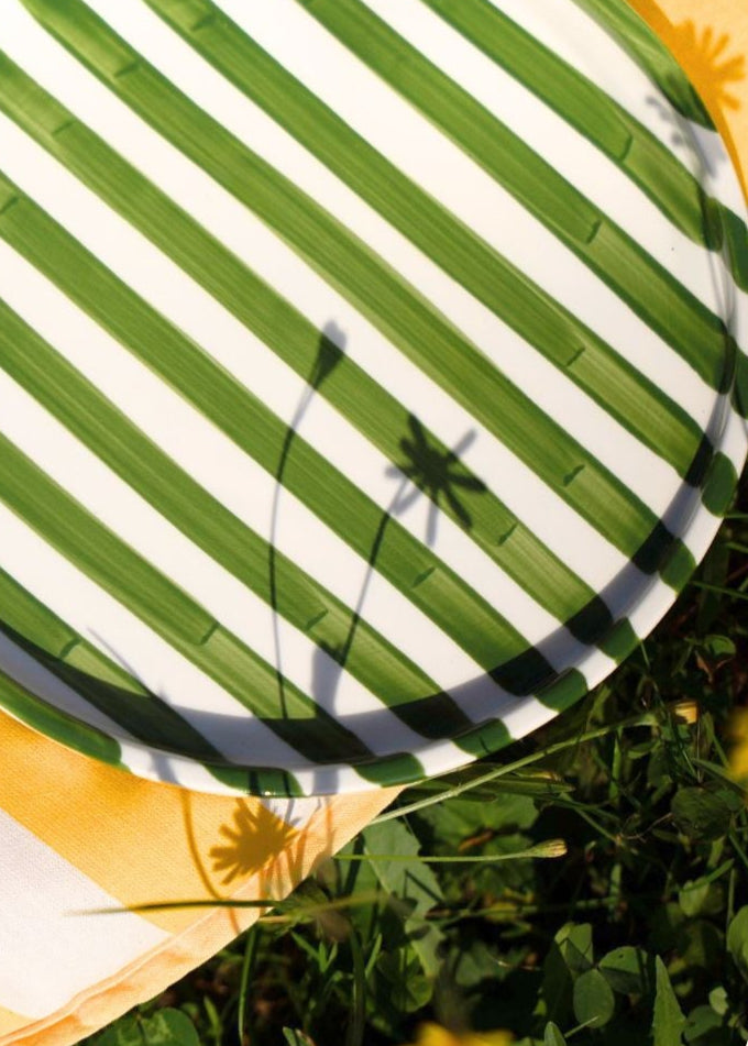 Green-White striped artisan handmade ceramic dinner plate on a yellow blanket on grass