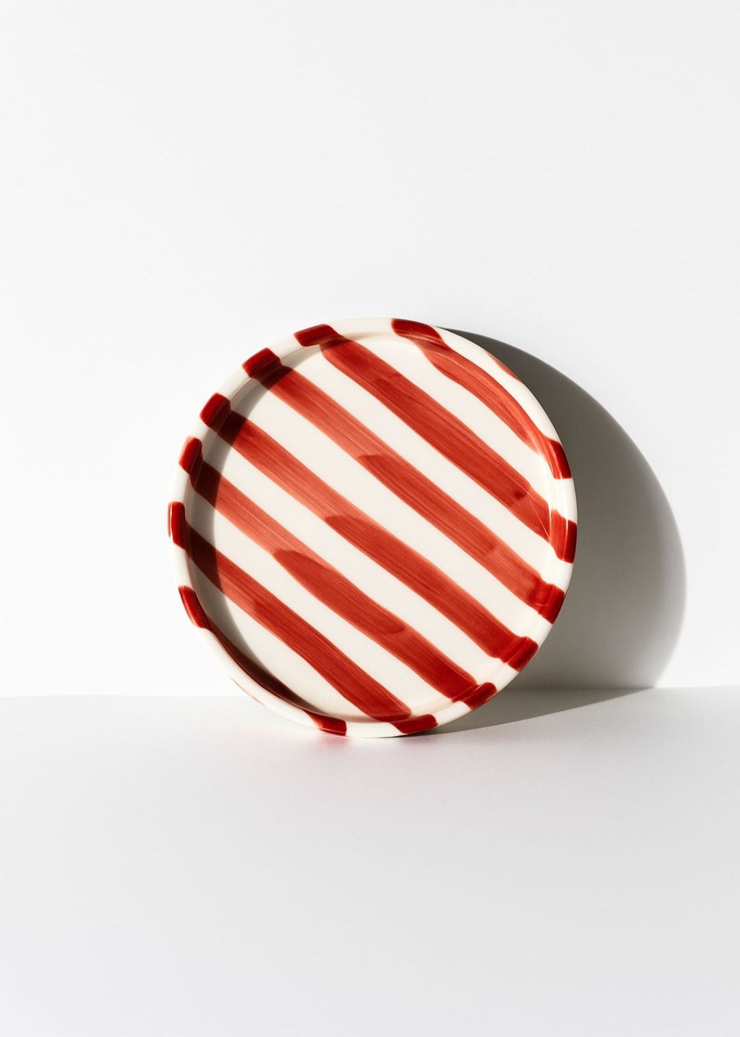 Round Artisan Ceramic Plate (Small) with red and white striped pattern on a beige background