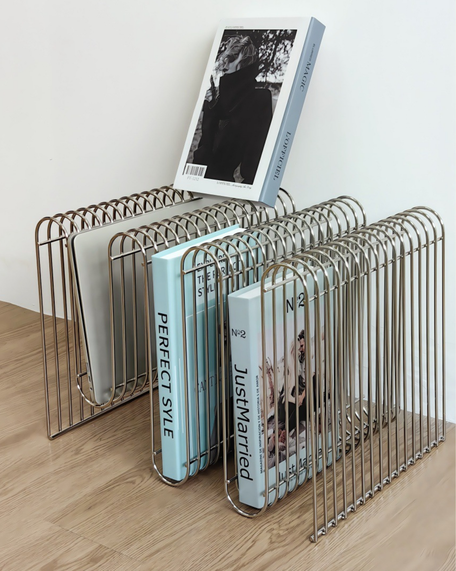 Metal magazine rack holding several books on a wooden surface with a white wall background