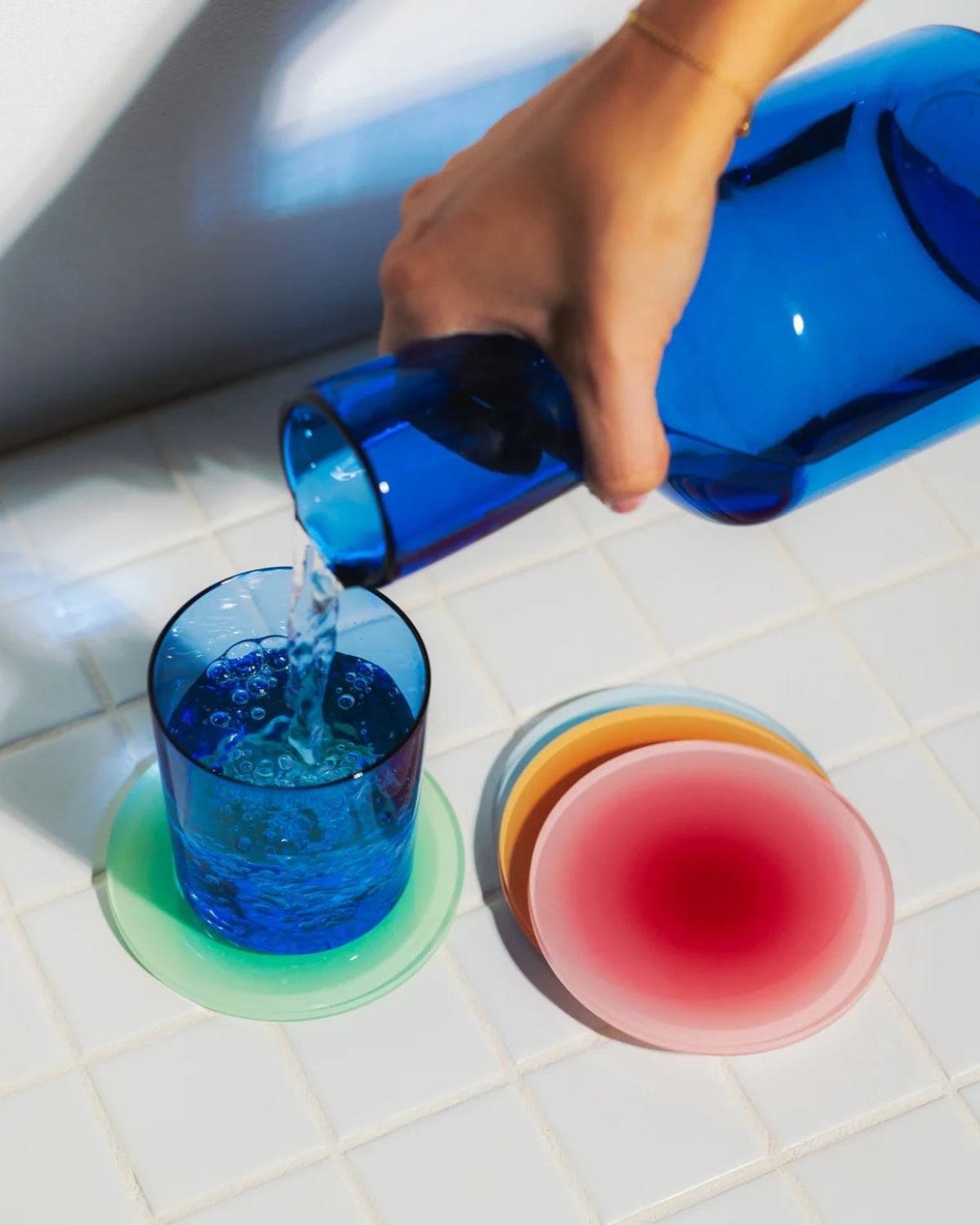 Colorful acrylic gradient coasters on white tiled surface with blue glass and bottle – modern aesthetic drinkware and kitchen accessories - Vibehaus