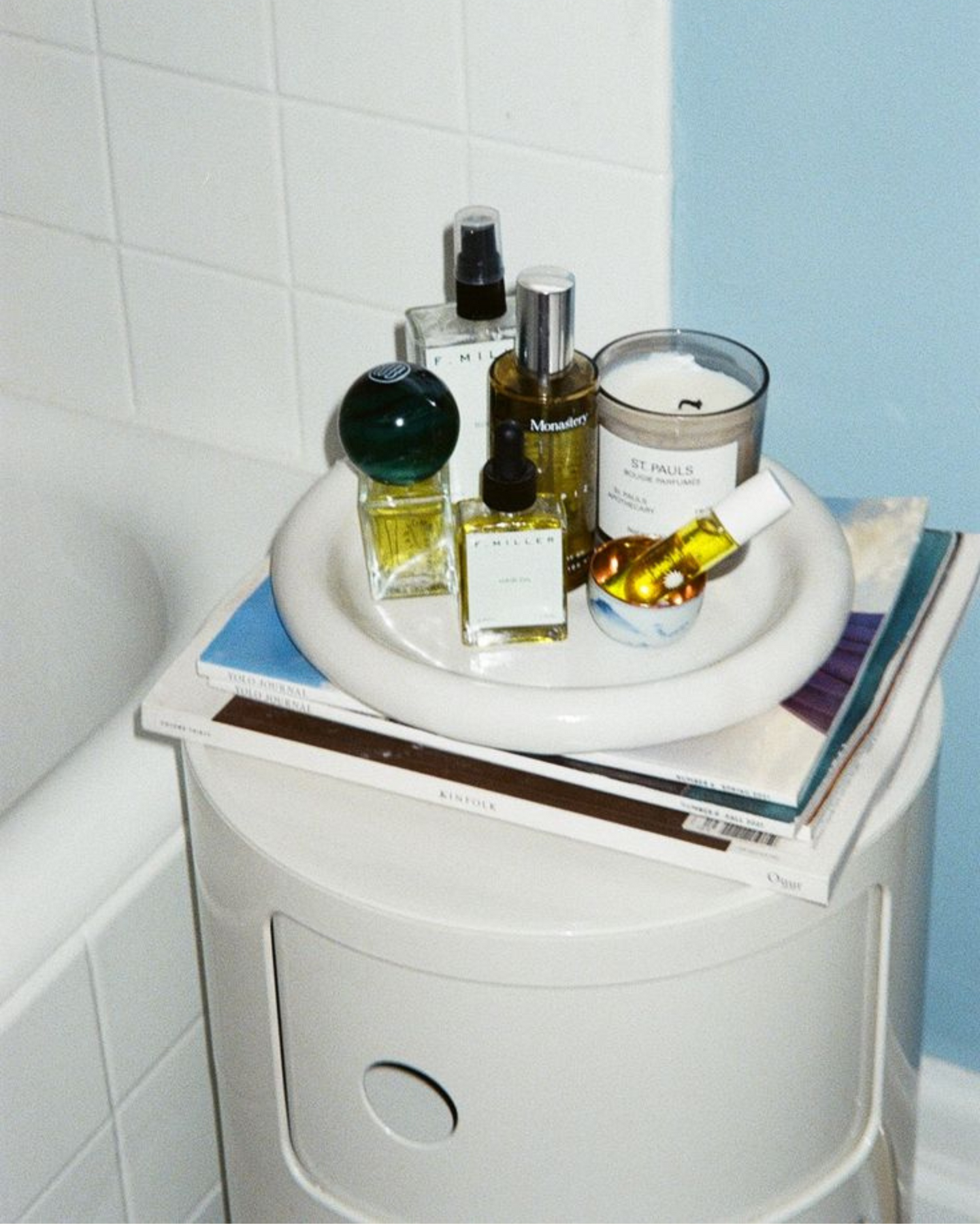 Perfume bottles and a candle on a white Componibili Storage Unit Replica cabinet in a bathroom setting