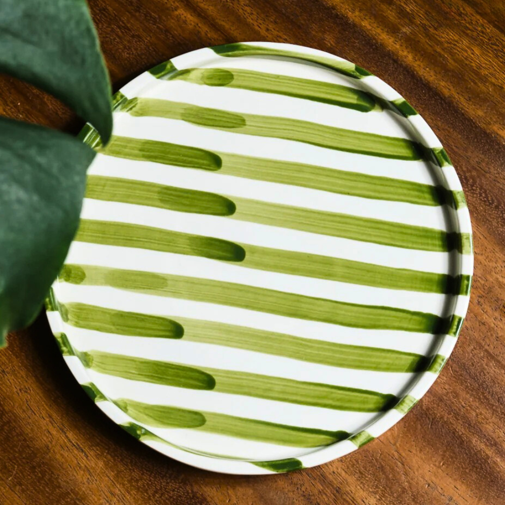 Green and white striped handmade artisan plate on a wooden surface