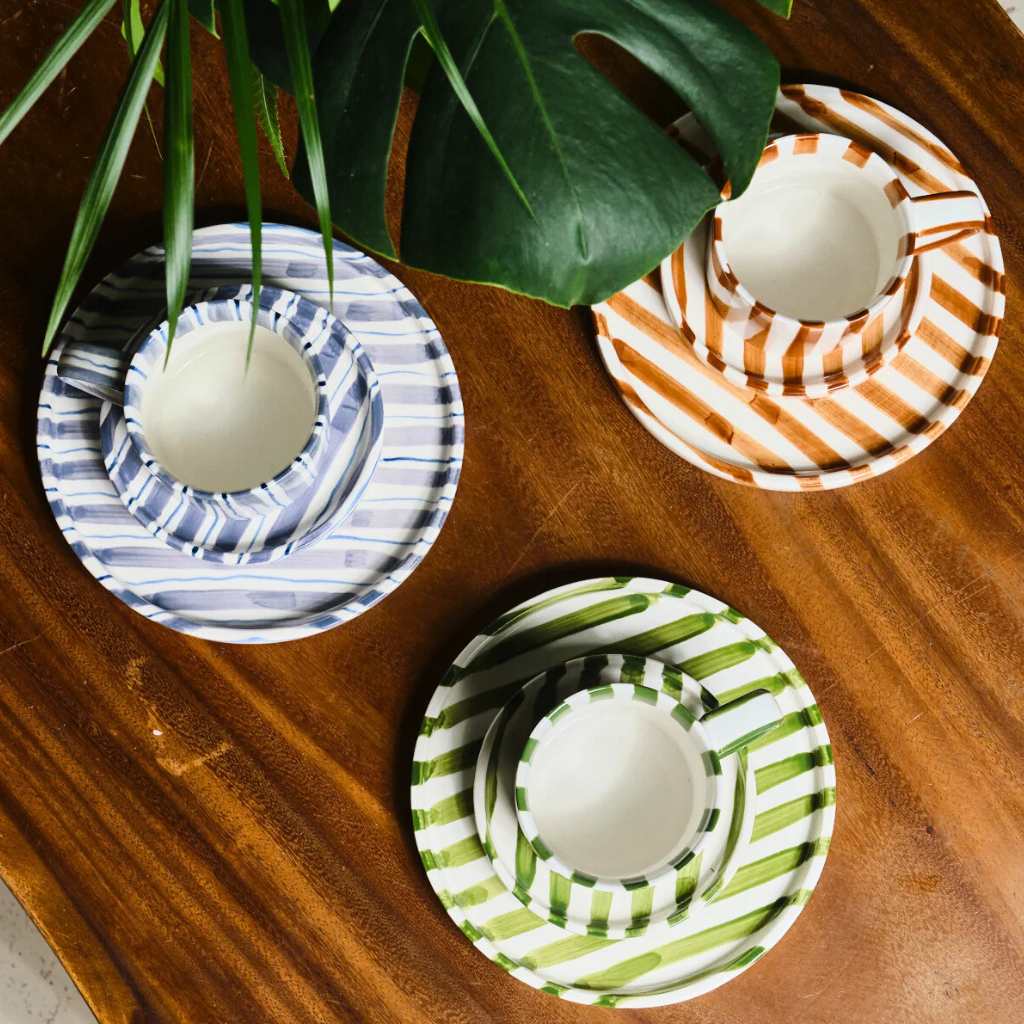 Three striped ceramic plate sets on a wooden surface with a plant leaf in the corner.