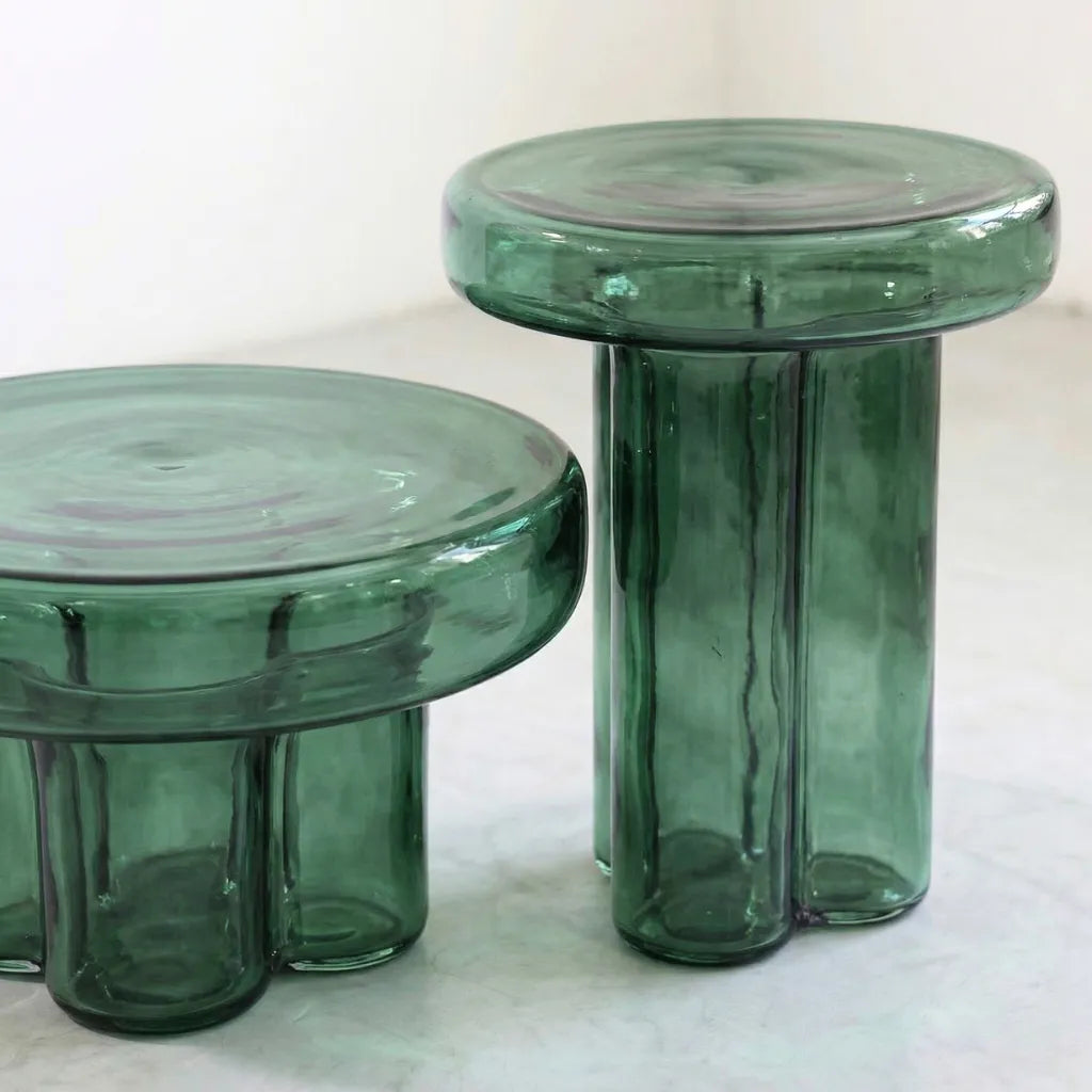 Two green round glass side tables on a concrete floor.