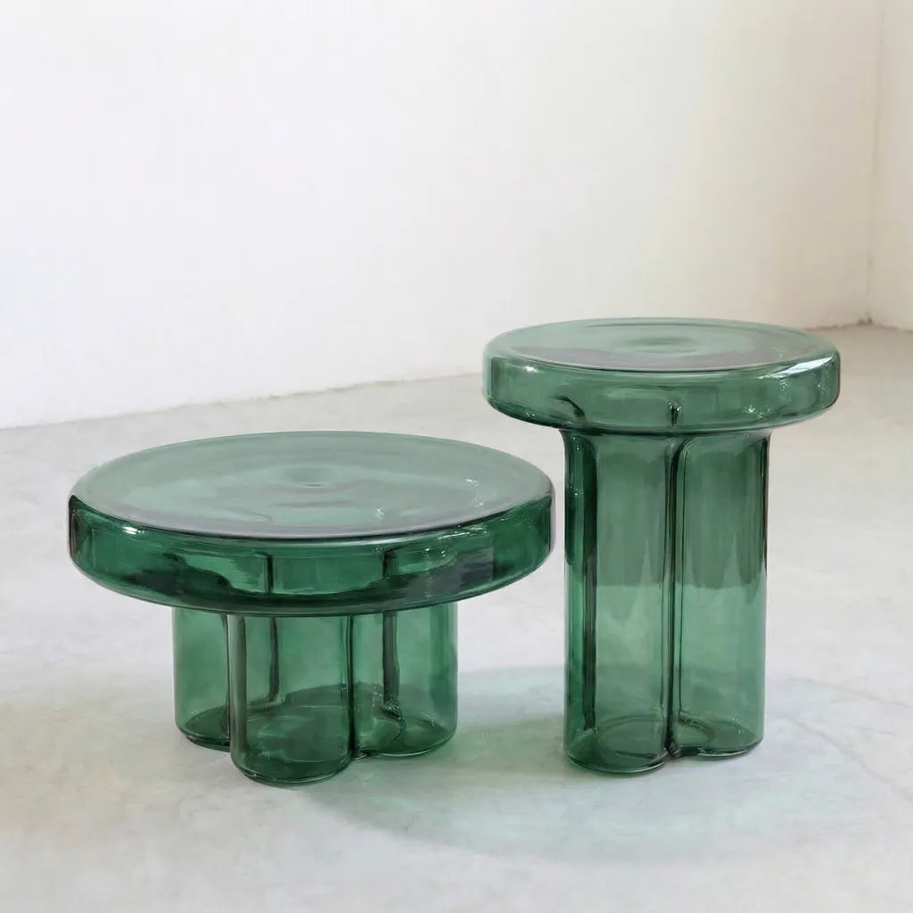Two green round glass side tables on a concrete floor.
