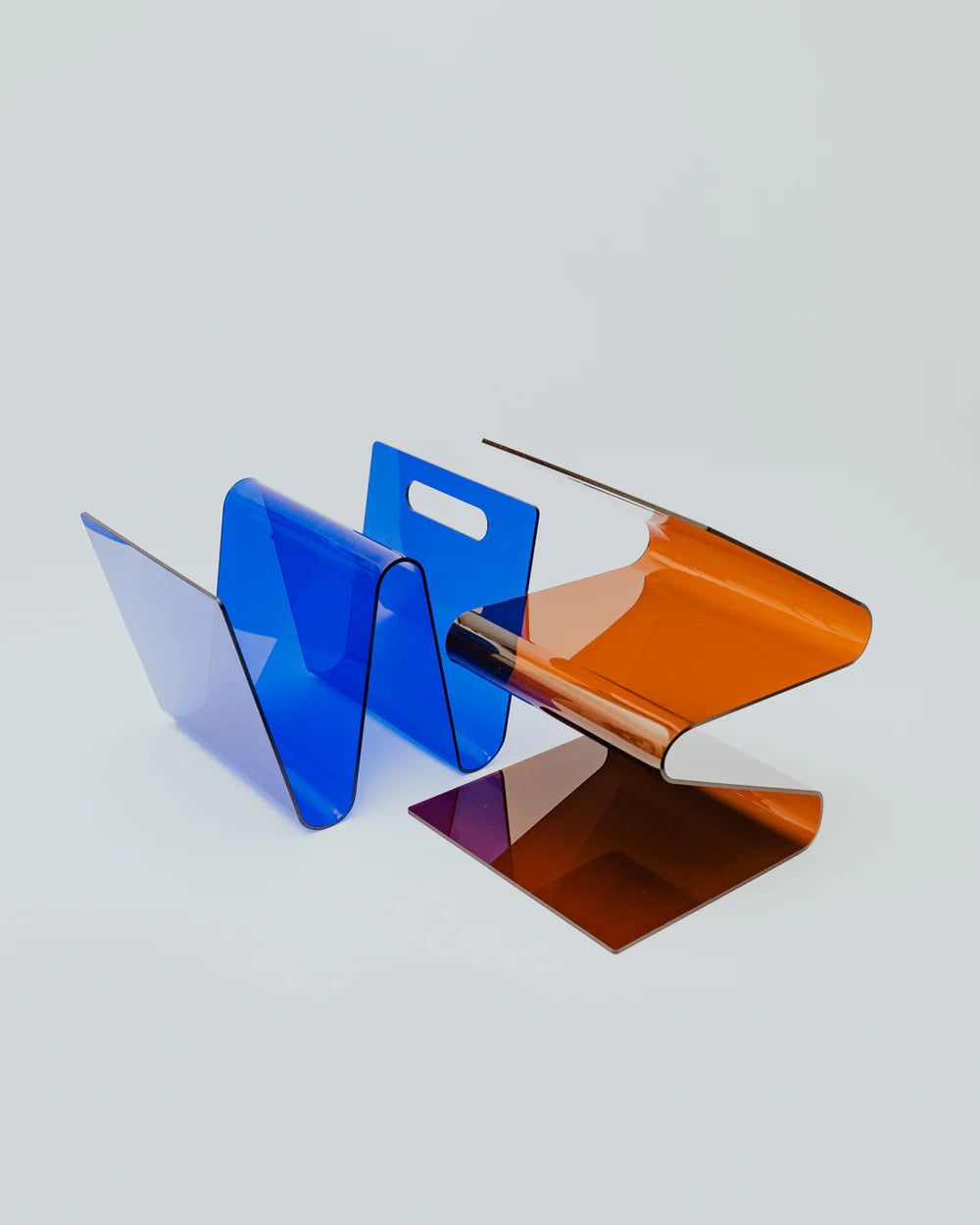 Two acrylic magazine racks in amber and blue on a light gray background