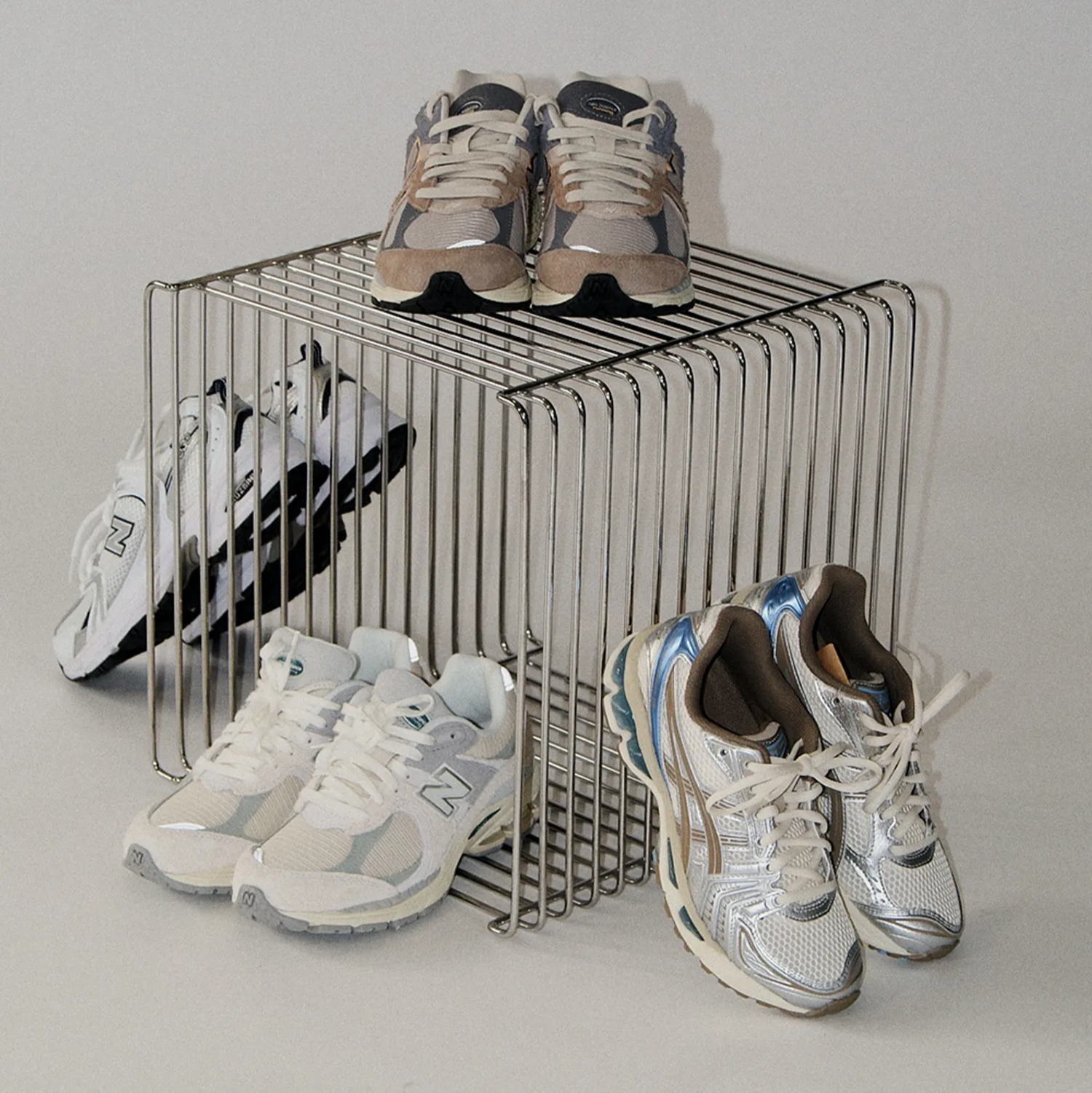 Modern wire side table made of chrome, shown on a minimalist beige background. Stackable cube design with clean geometric lines. Used as shoe storage for new balance.