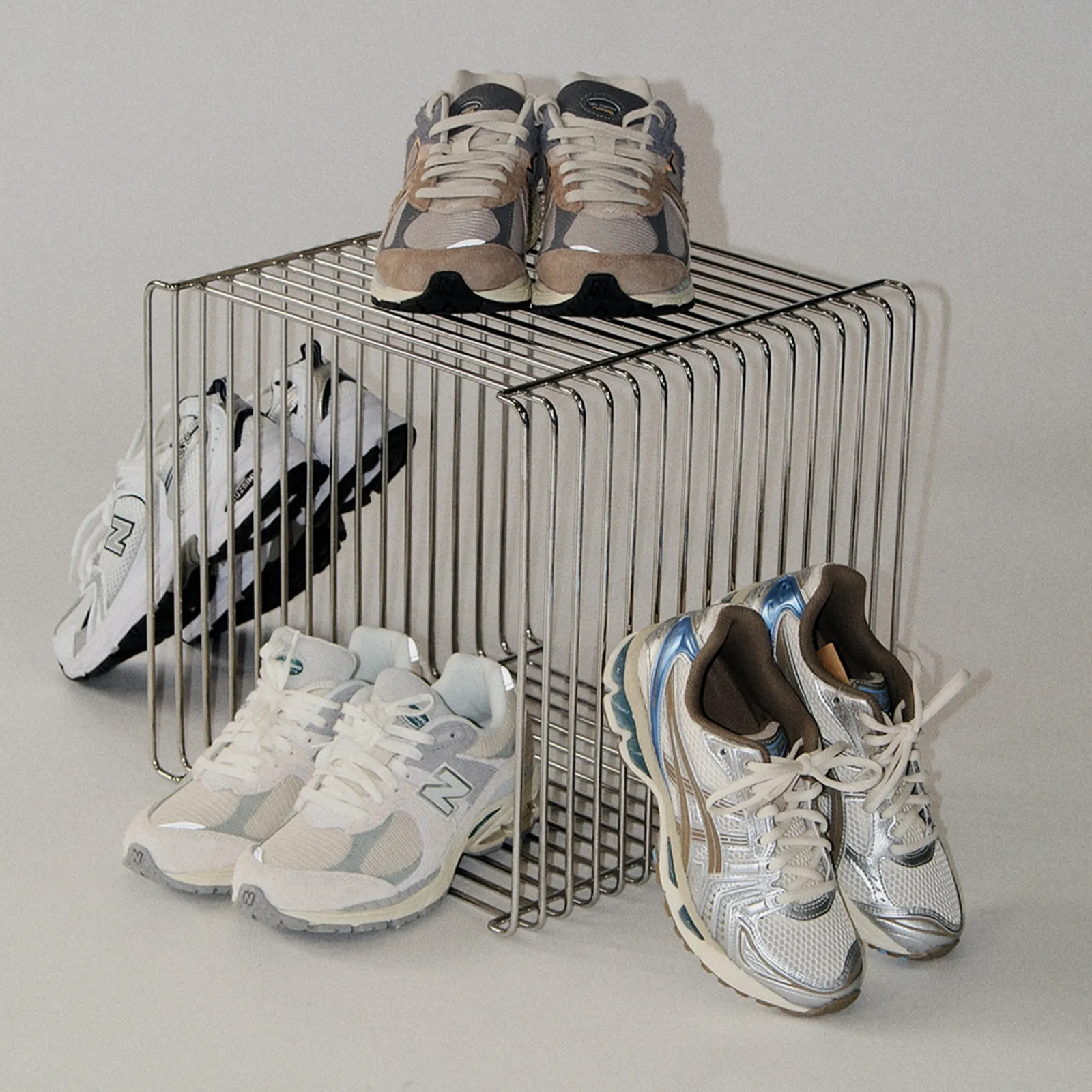 Modern wire side table made of chrome, shown on a minimalist beige background. Stackable cube design with clean geometric lines. Used as shoe storage for new balance.