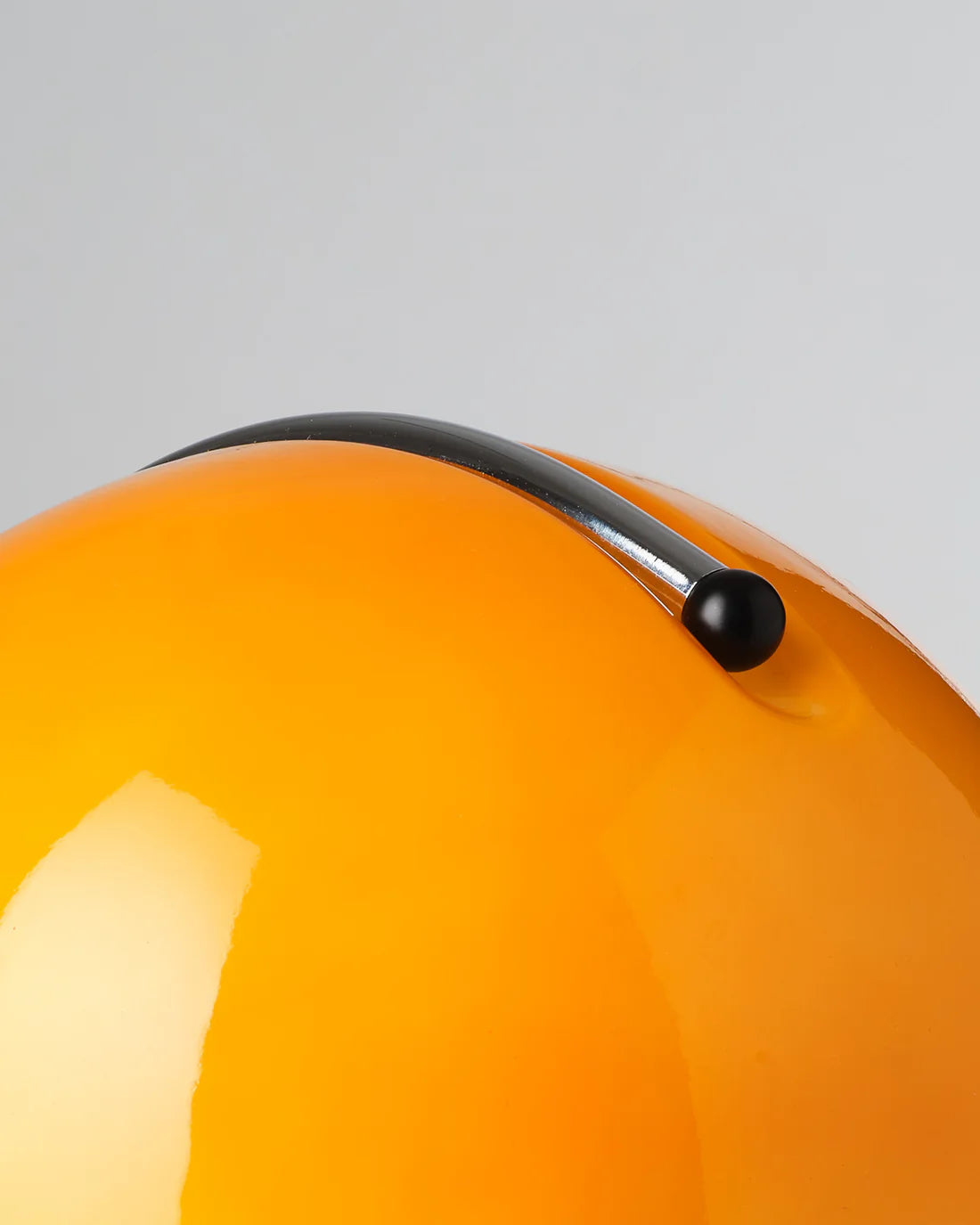 Close-up of an orange aromatherapy lamp with a chrome strap on a gray background