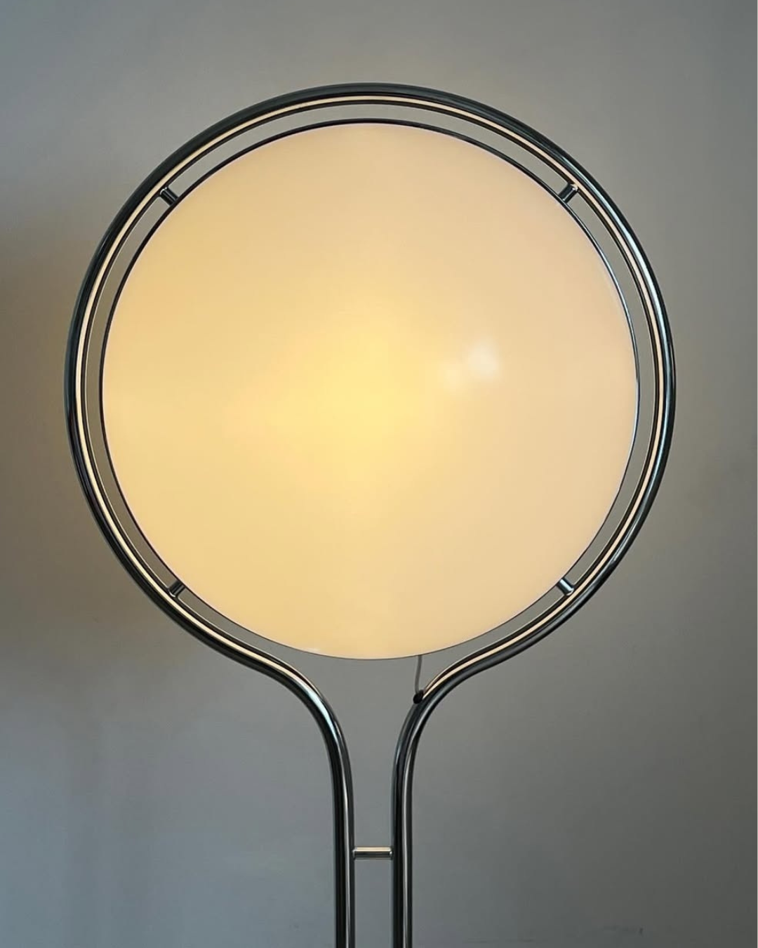 Gulvkuglelampe med rund glasskærm og metallisk ramme på grå baggrund