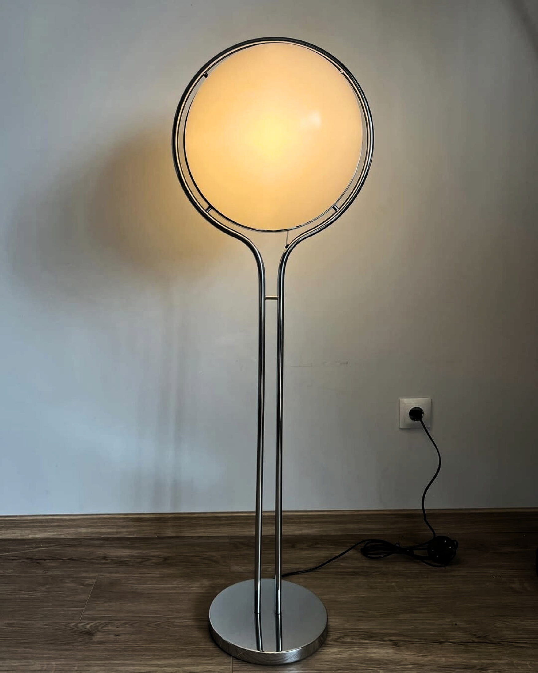 Globe Floor lamp with a round glass shade on a wooden floor against a plain wall.
