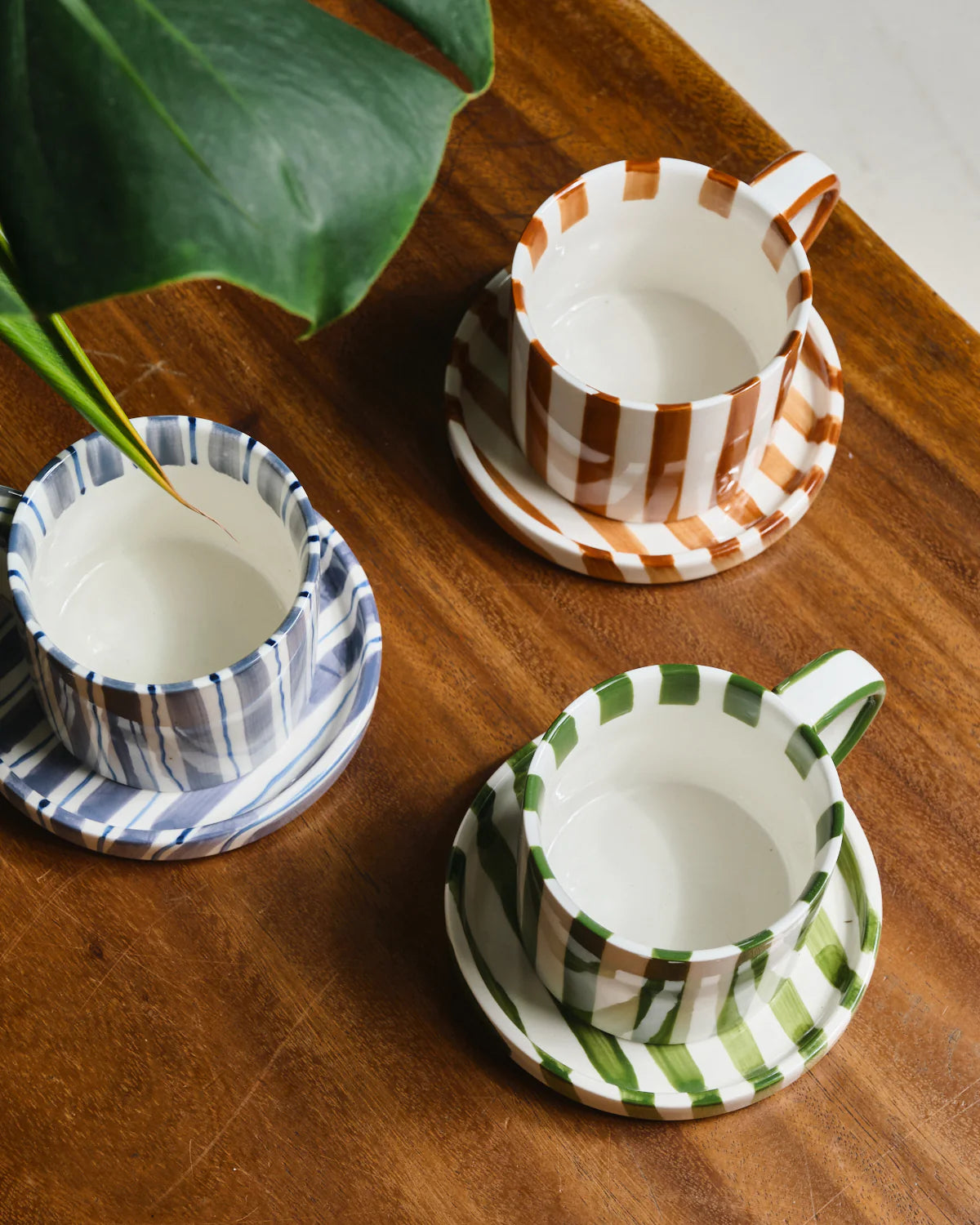 Three striped ceramic cups with saucers on a wooden surface, each featuring different patterns.