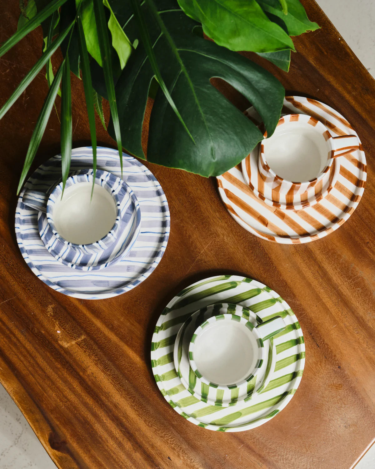 Three striped ceramic cups with saucers on a wooden surface, each featuring different patterns.
