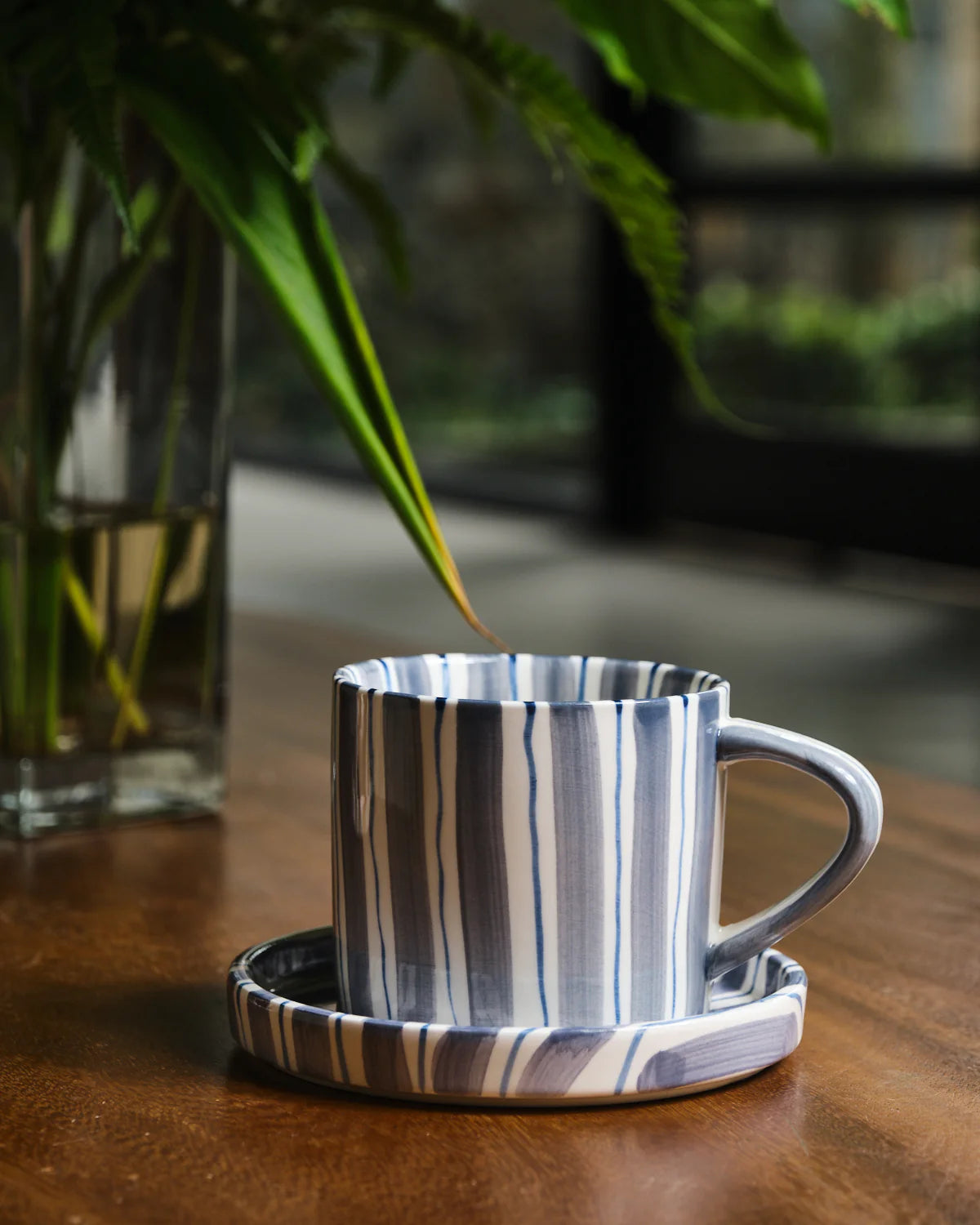 Striped ceramic mug on a matching coaster with a blurred plant in the background