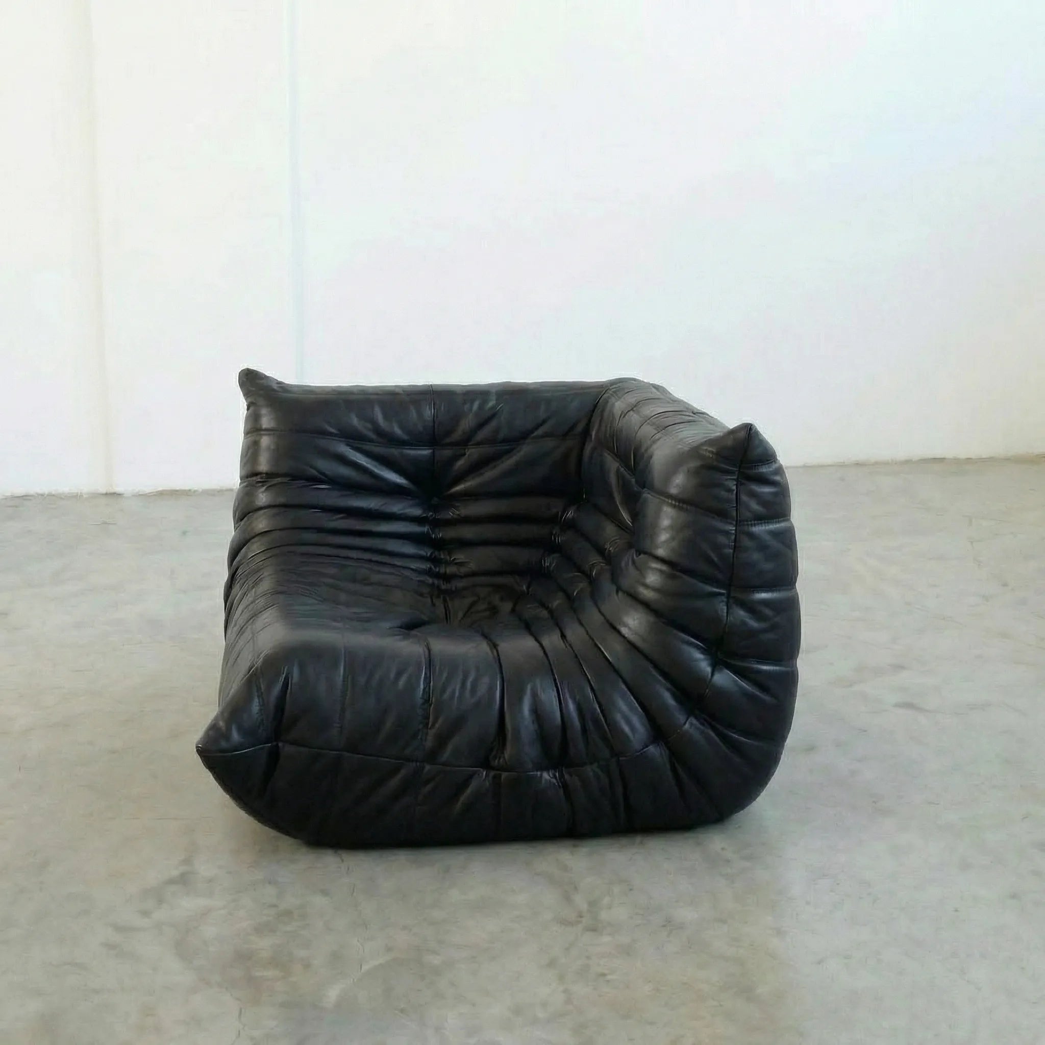 Togo Corner Section Dupe in black leather on a concrete floor with a white wall background