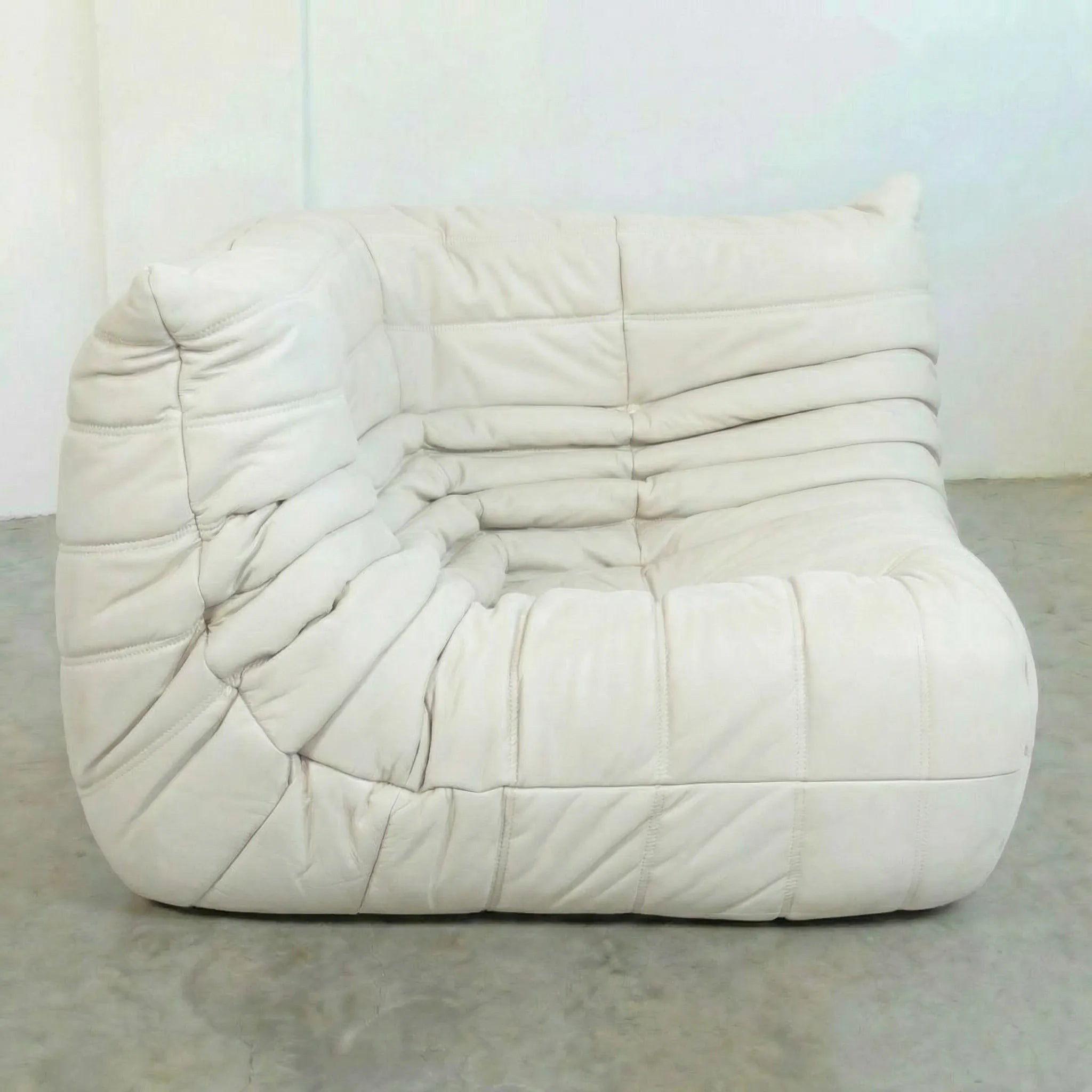 Togo Corner Section Dupe in white leather on a concrete floor with a white wall background
