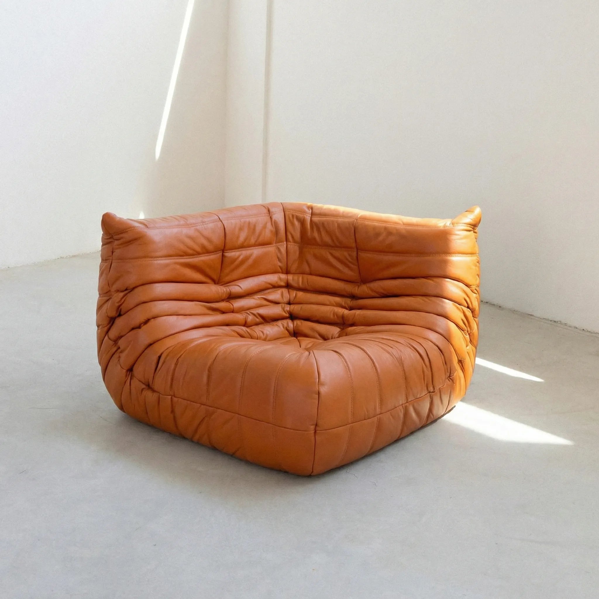 Togo Corner Section Dupe in cognac leather on a concrete floor with a white wall background