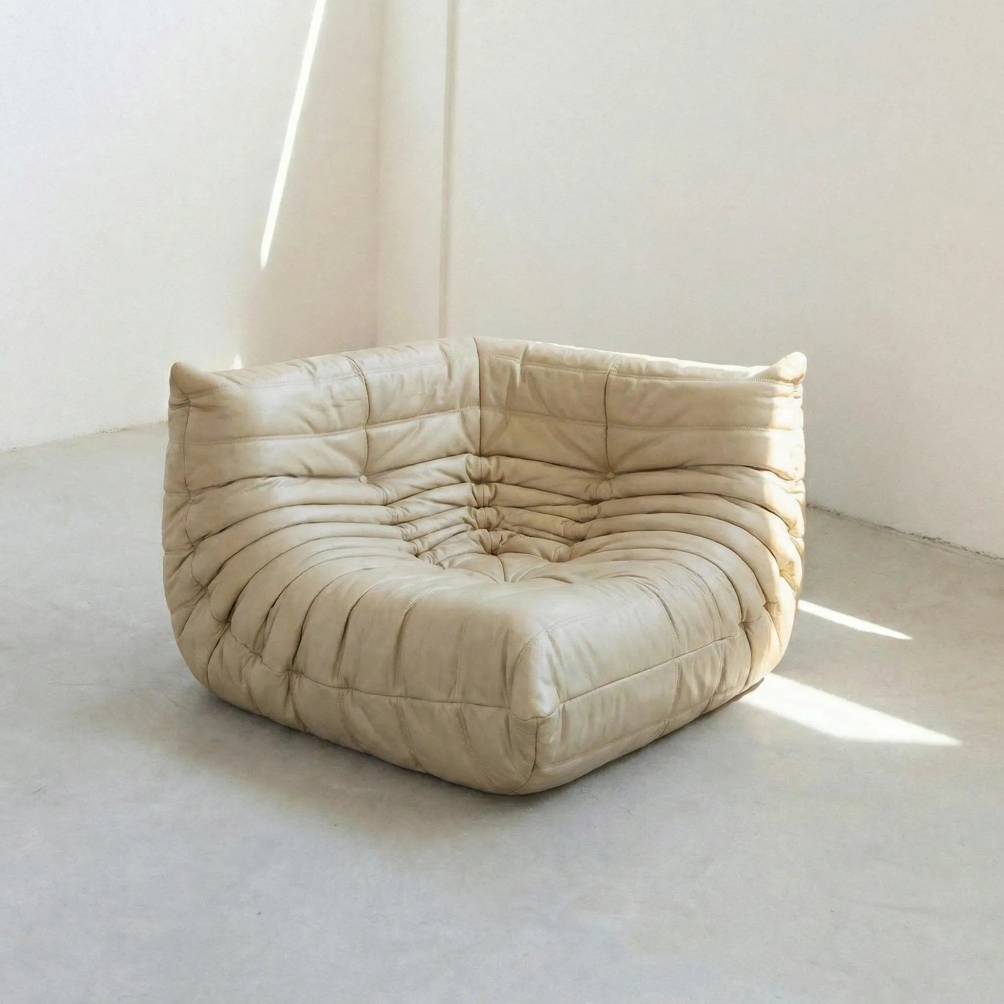 Togo Corner Section Dupe in beige leather on a concrete floor with a white wall background