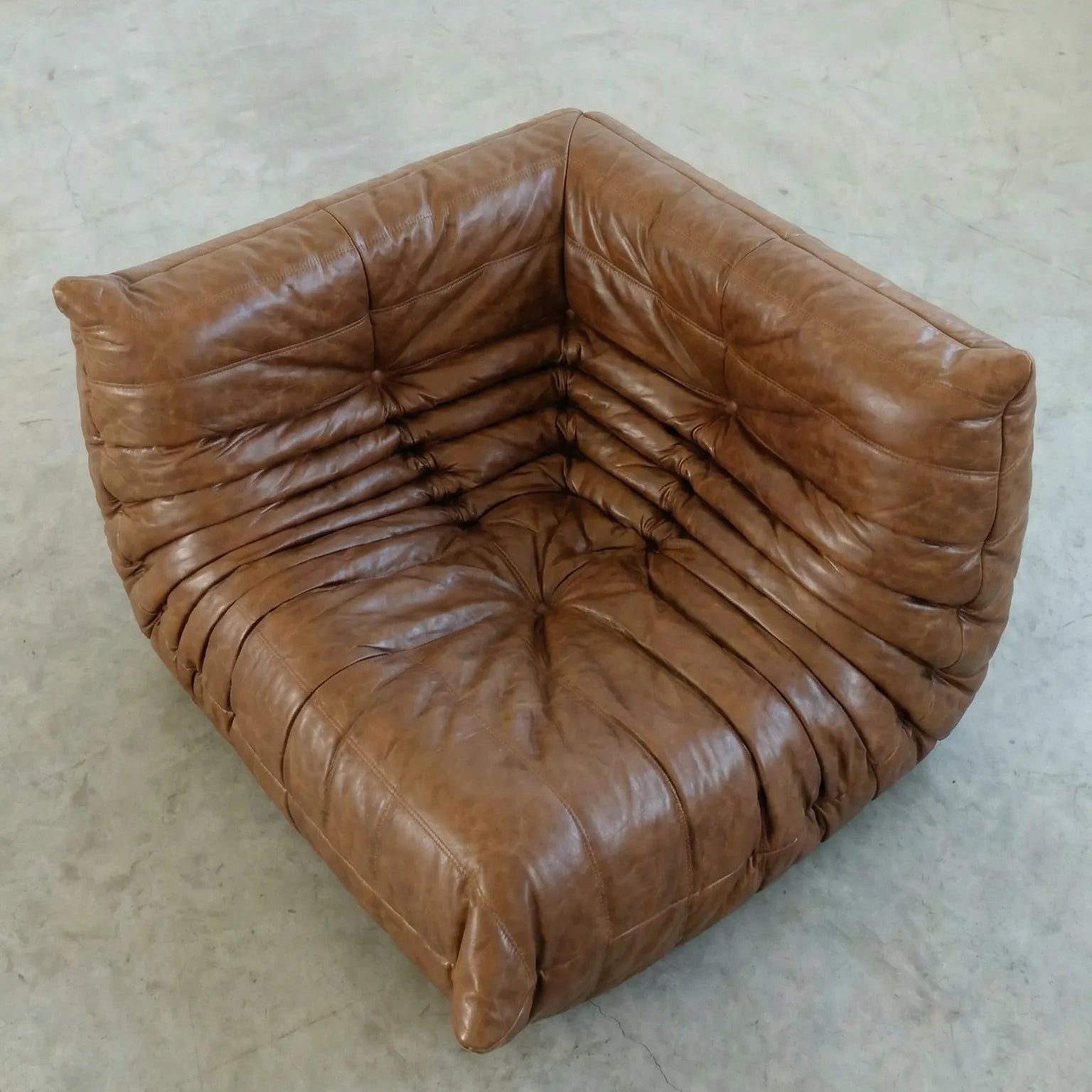 Togo Corner Section Dupe in brown leather on a concrete floor with a white wall background