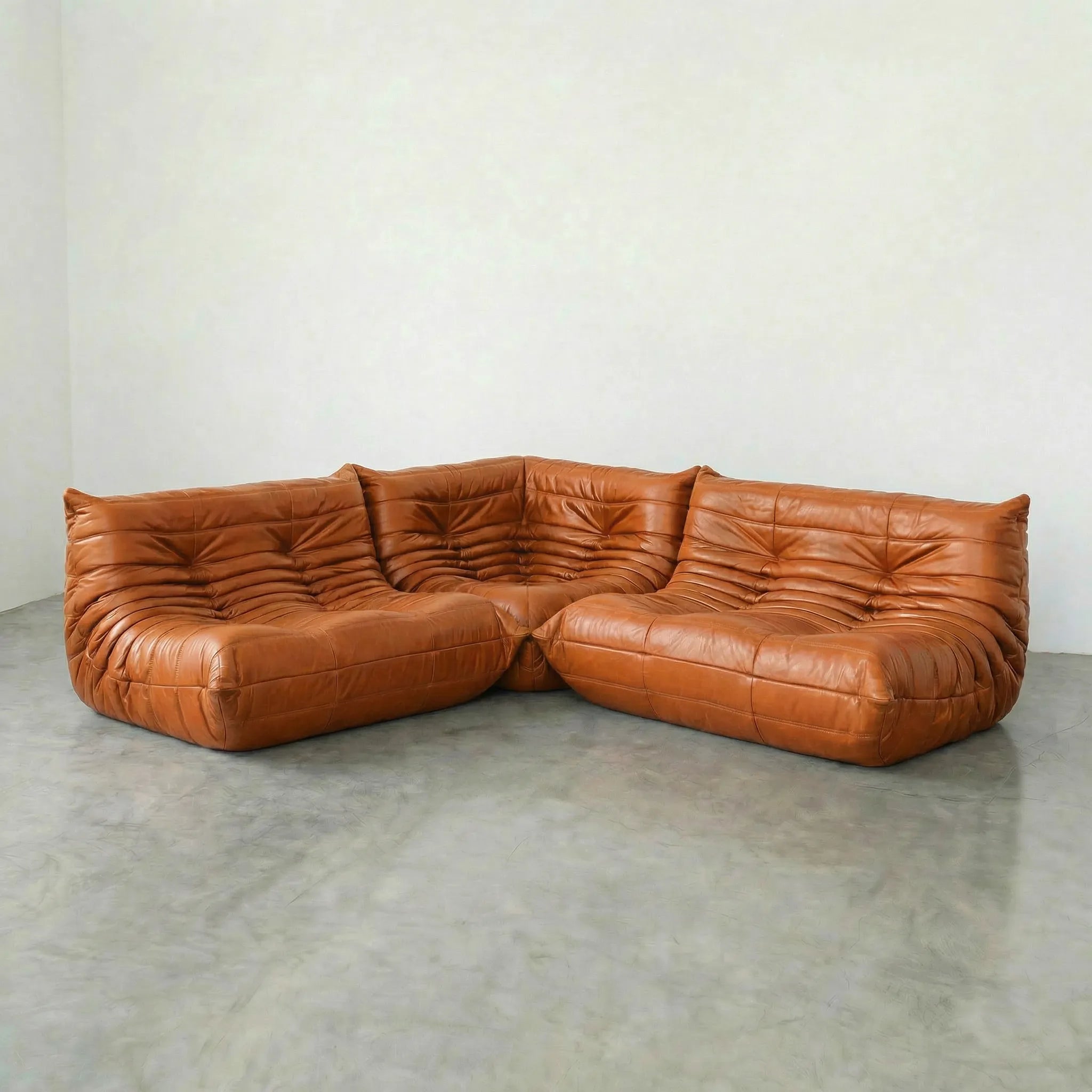 Cognac leather togo sectional sofa dupes on a concrete floor with a white wall background