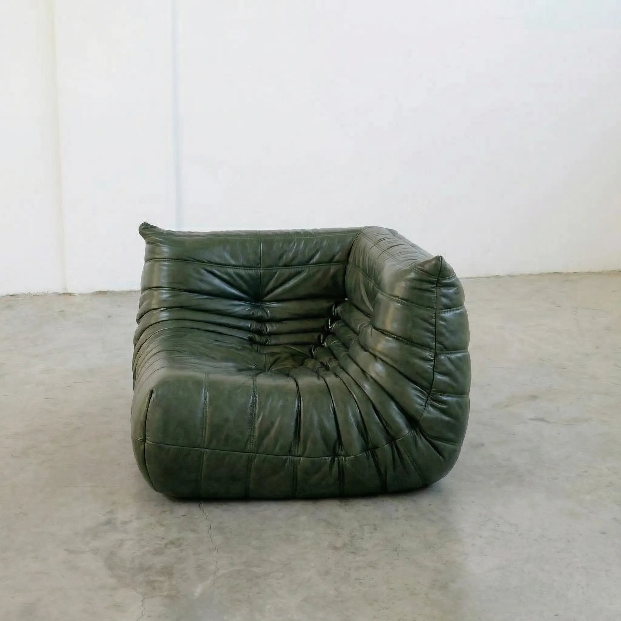Green togo leather chair on a concrete floor with a white wall background