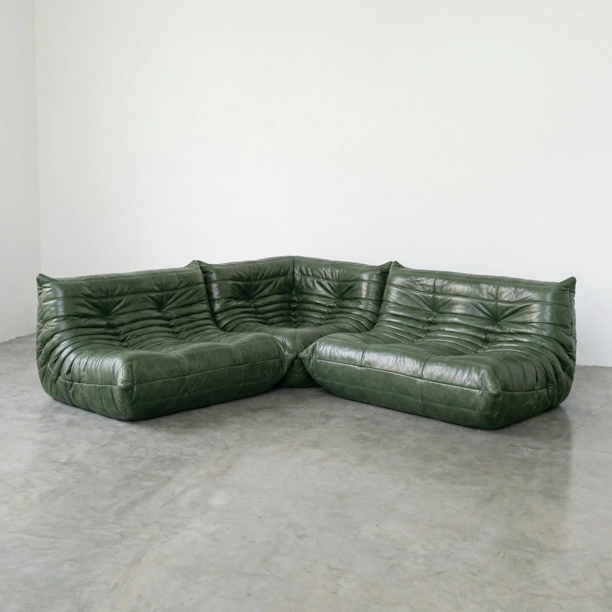 Green leather togo sectional sofa dupes set on a concrete floor with a white wall background