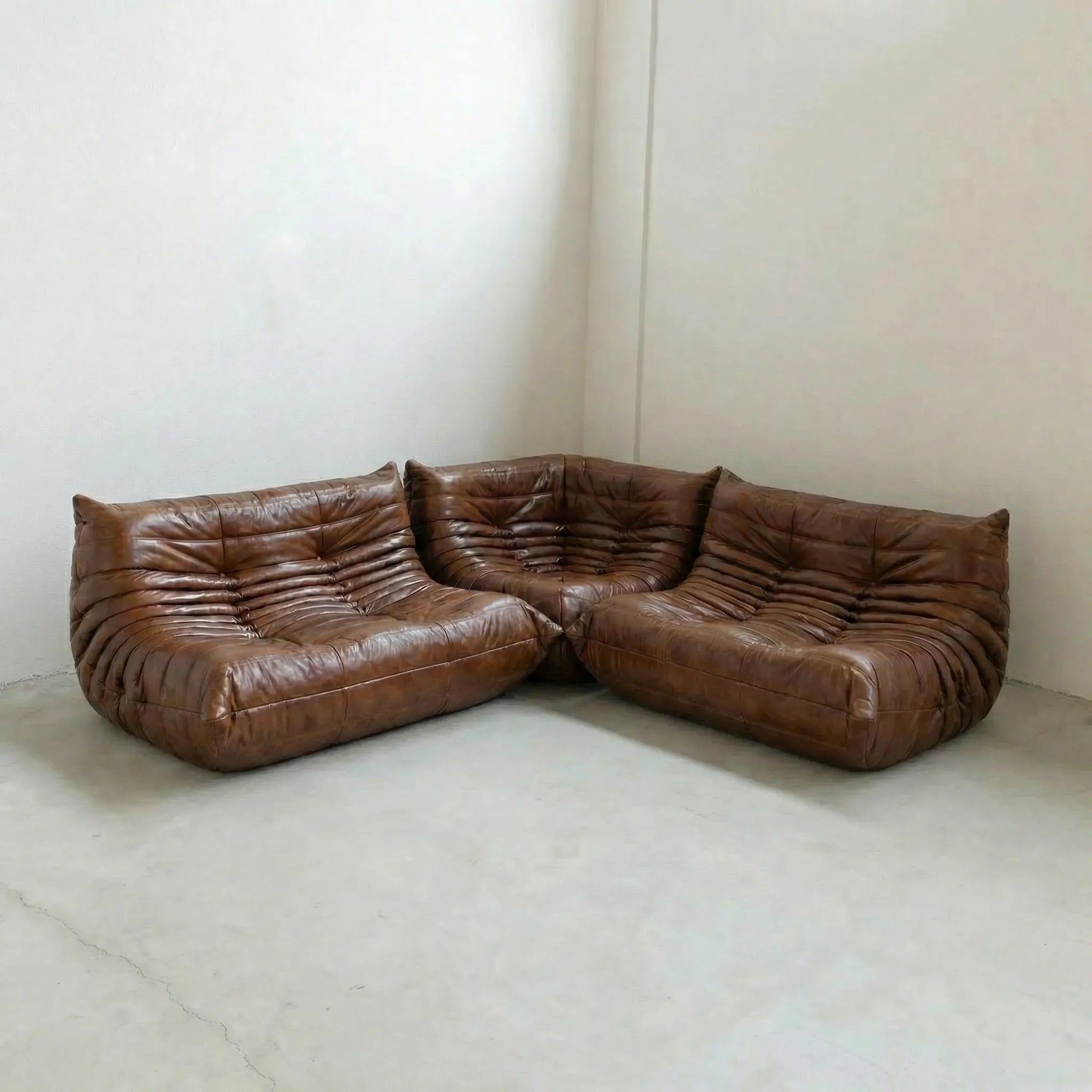 Brown leather togo set sectional sofa dupes on a concrete floor with a white wall background
