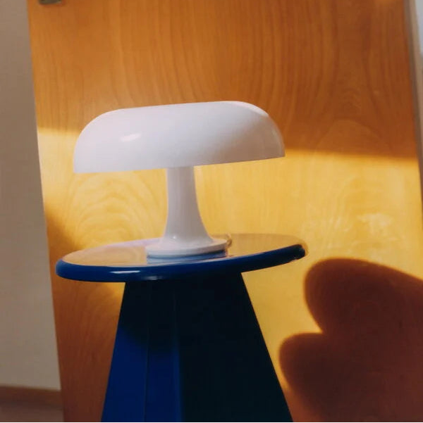 White Bella lamp on a blue stand against a wooden door