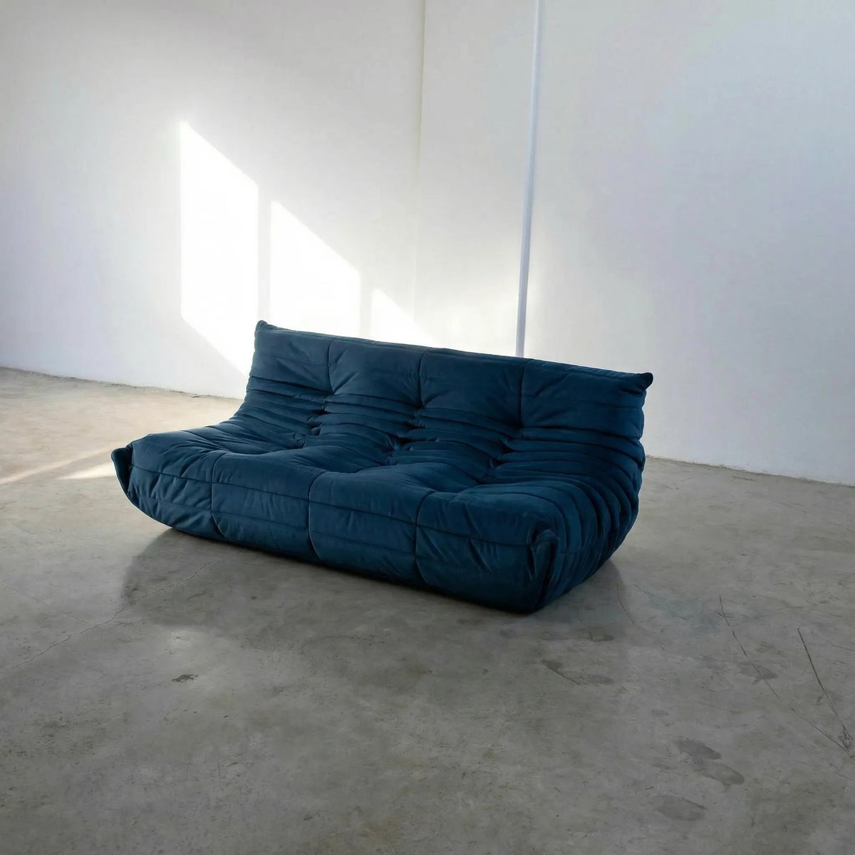 Bruma 3 seater sofa in dark blue Velvet Suede by vibehaus on a concrete floor, photographed from a side angle.