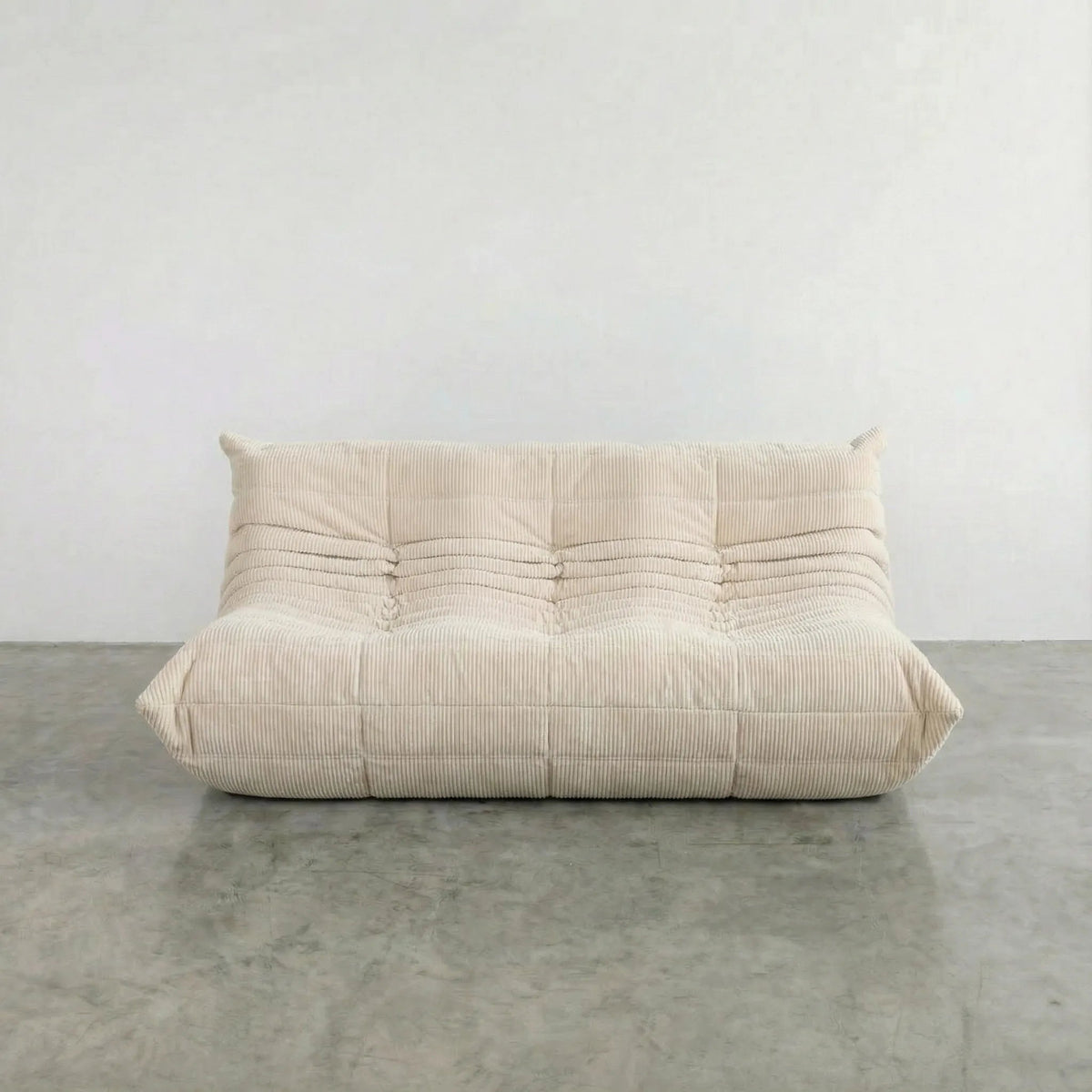 Bruma 3 seater sofa in cream Corduroy by vibehaus on a concrete floor, photographed from a front angle.