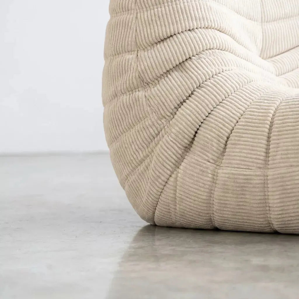 Close up of the bottom corner of the Bruma 3 seater sofa in cream Corduroy by vibehaus on a concrete floor