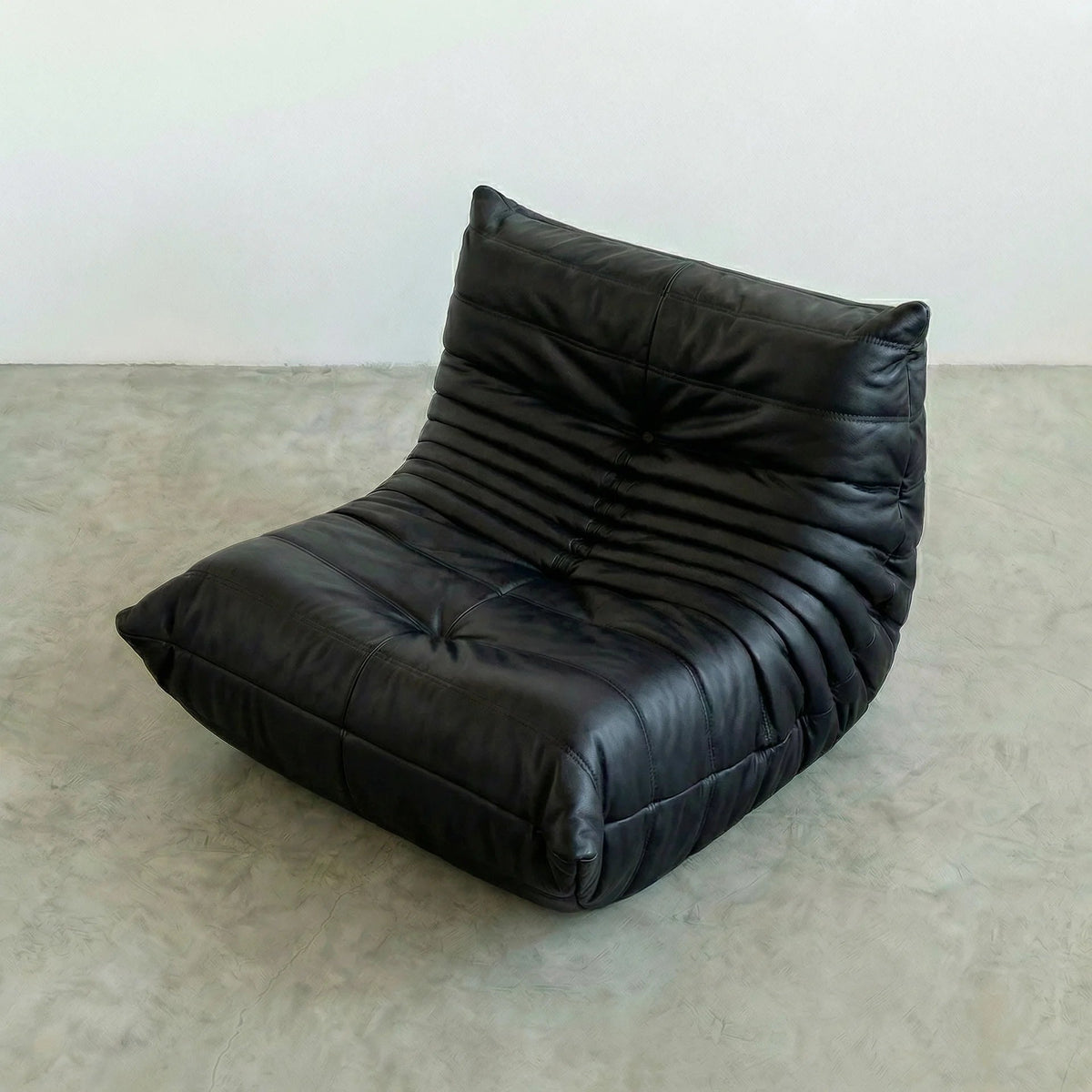 Bruma Chair in Black faux leather on a beige floor with a white wall background