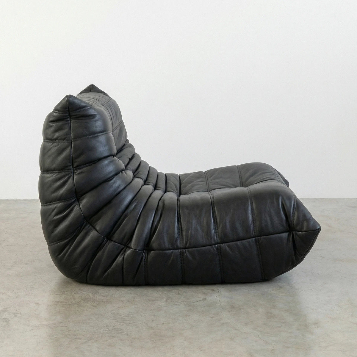 Bruma Chair in black real cowhide leather on a concrete floor with a white wall background hot from a side angle