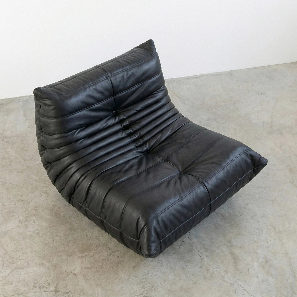 Bruma Chair in black real cowhide leather on a concrete floor with a white wall background