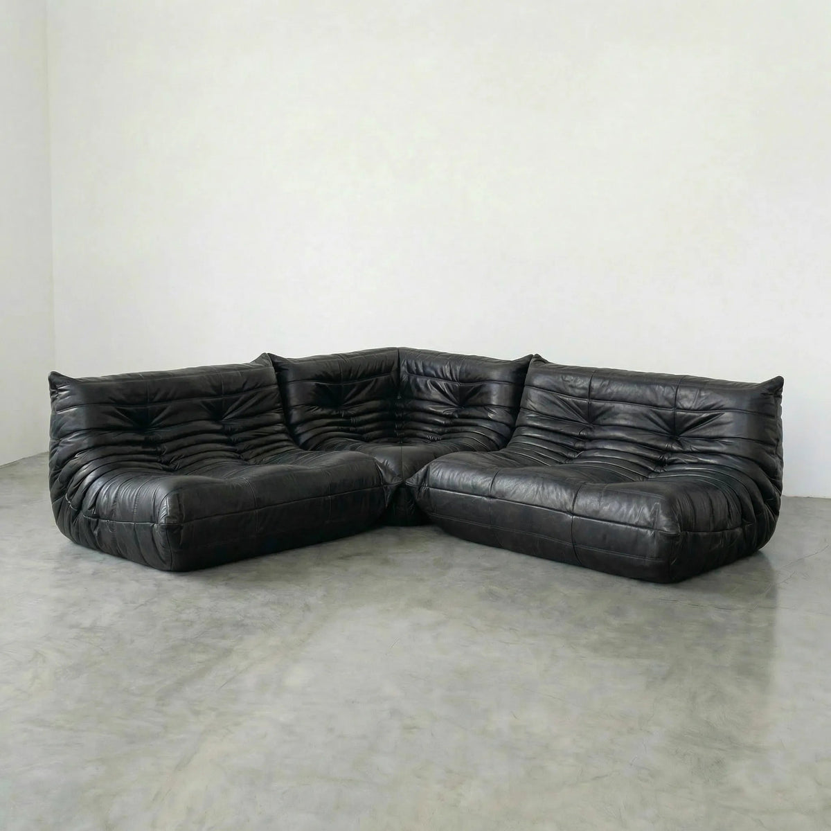 Black leather sectional Bruma sofa on a concrete floor with a white wall background