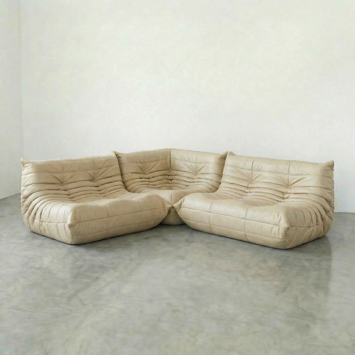 Cream Beige leather Bruma sectional sofa on a concrete floor with a white wall background