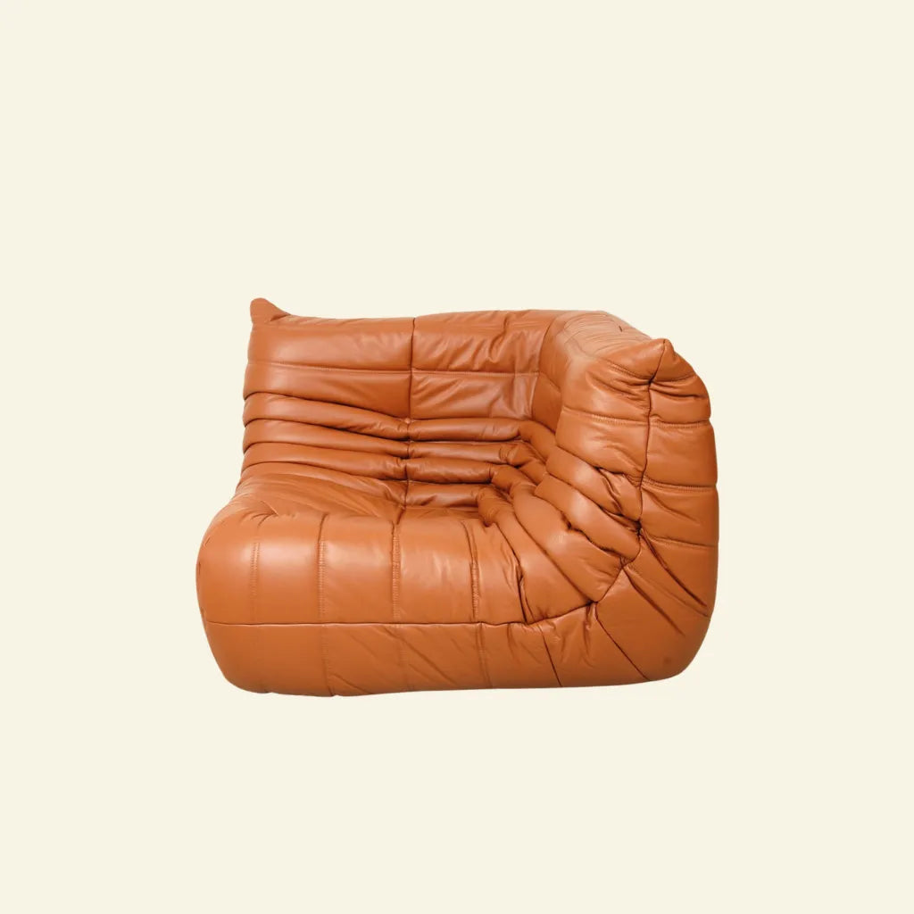 Bruma Corner Section in cognac leather on a concrete floor with a white wall background