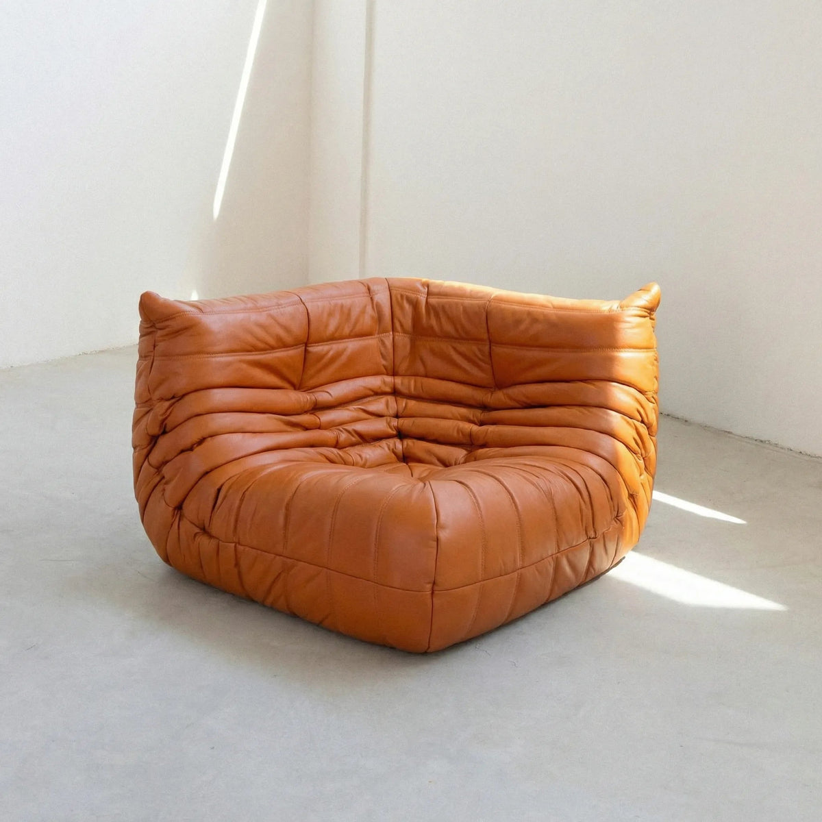 Bruma Corner Section in cognac leather on a concrete floor with a white wall background