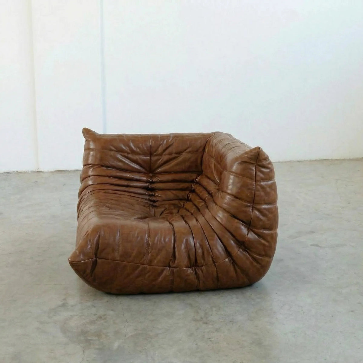 Bruma Corner Section in brown leather on a concrete floor with a white wall background