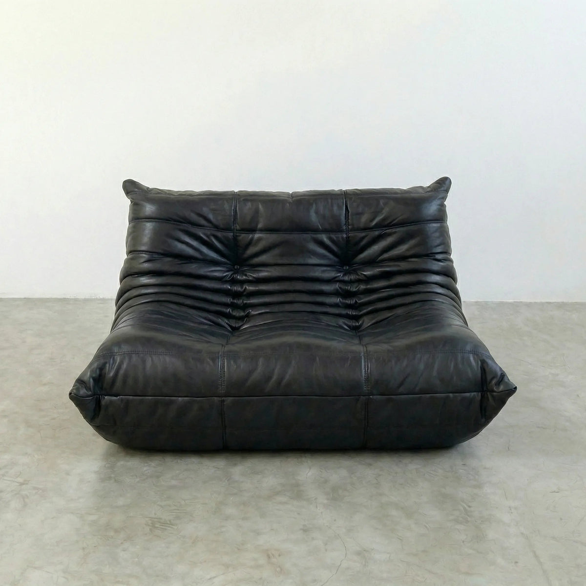 Bruma sofa in black leather on a concrete floor with a white wall background
