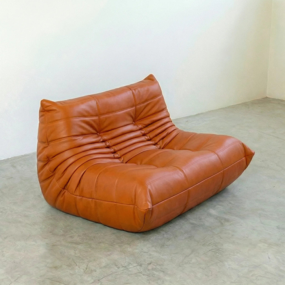Orange leather Bruma sofa on a concrete floor with a white wall background
