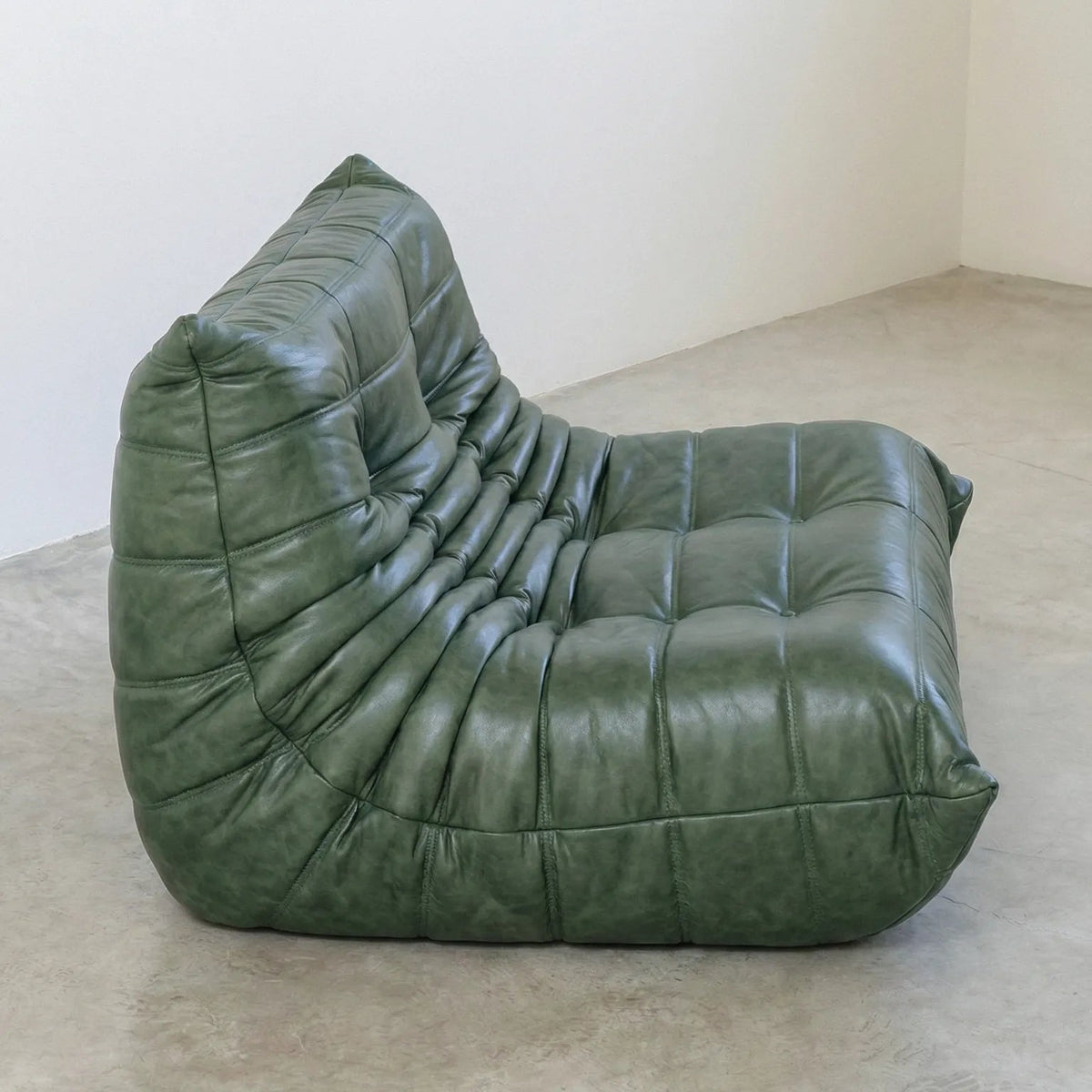 Green Bruma sofa in leather on a concrete floor with a white wall background