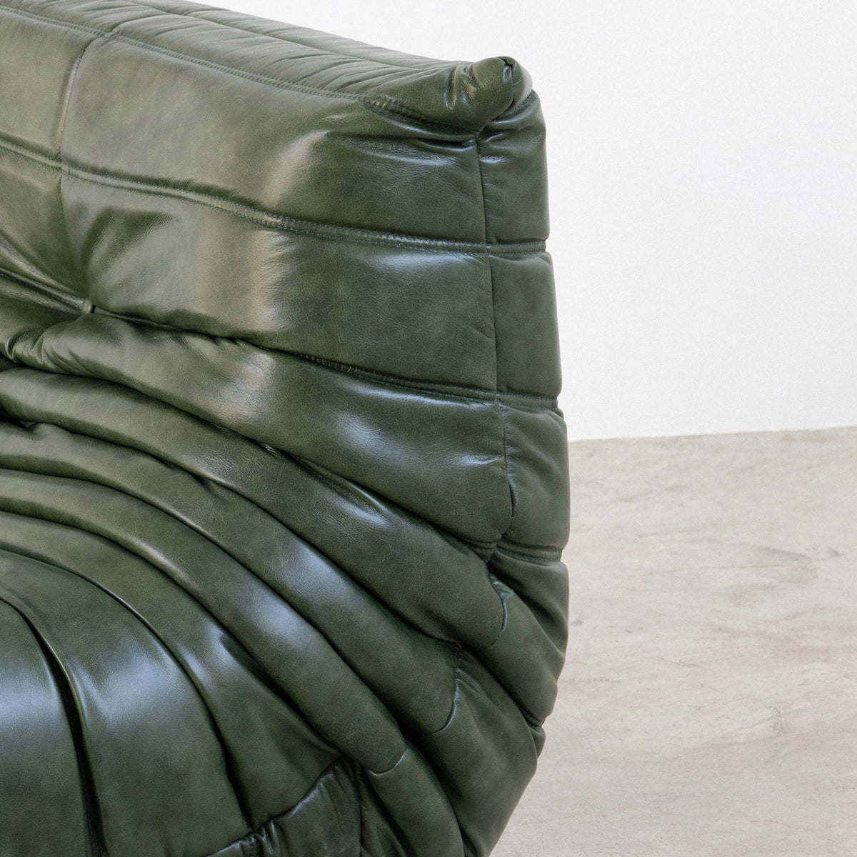 Close-up of the Bruma Chair in green real shiny oil wax leather on a concrete floor with a white wall background