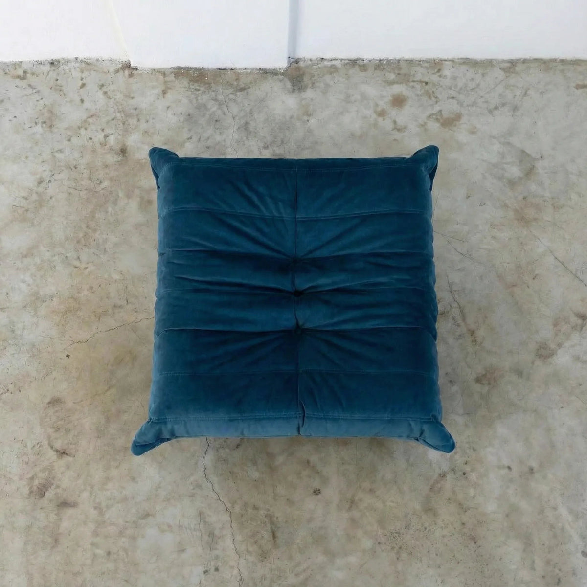 Dark blue Bruma ottoman in velvet suede on a concrete floor.