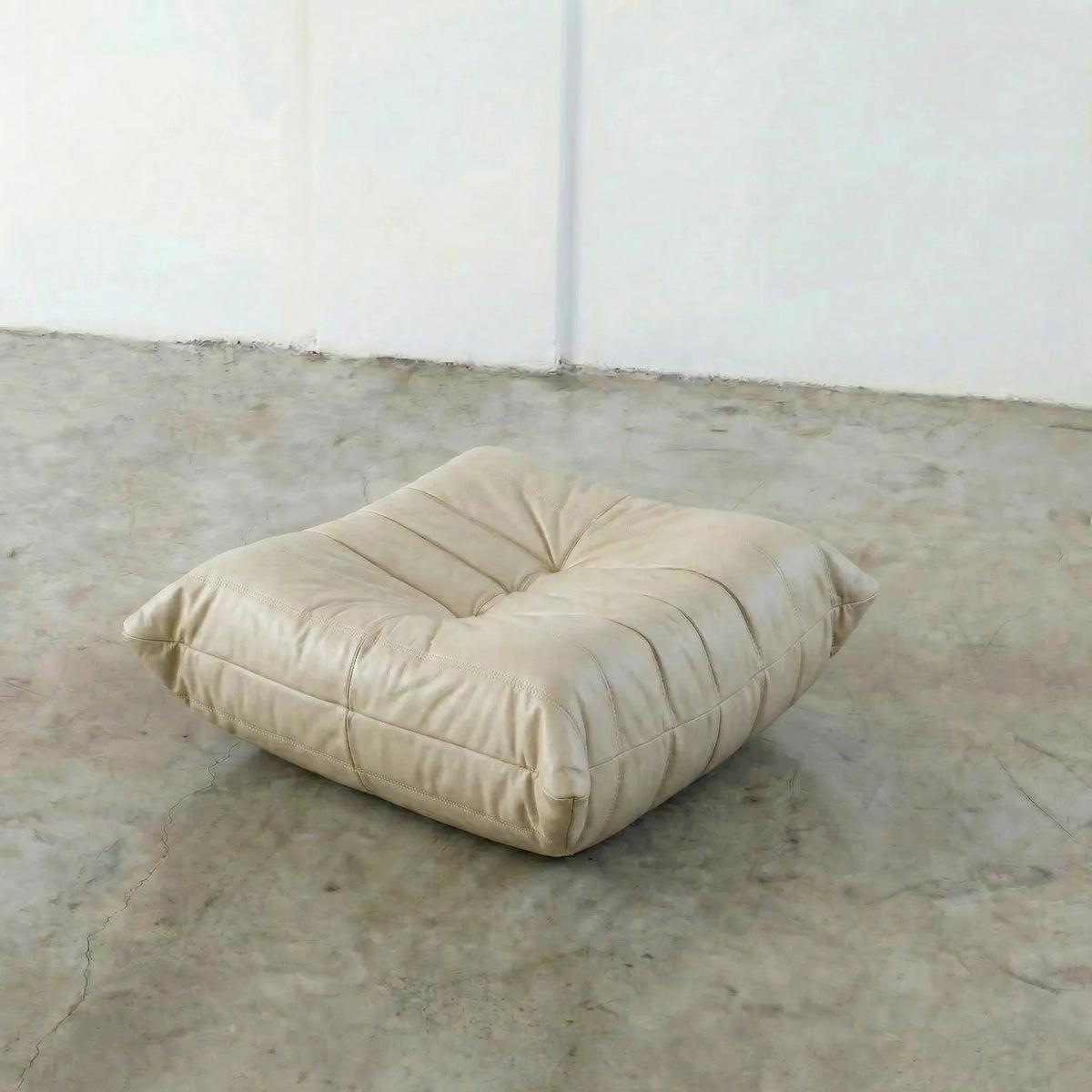 Beige Bruma leather ottoman on a concrete floor with white walls