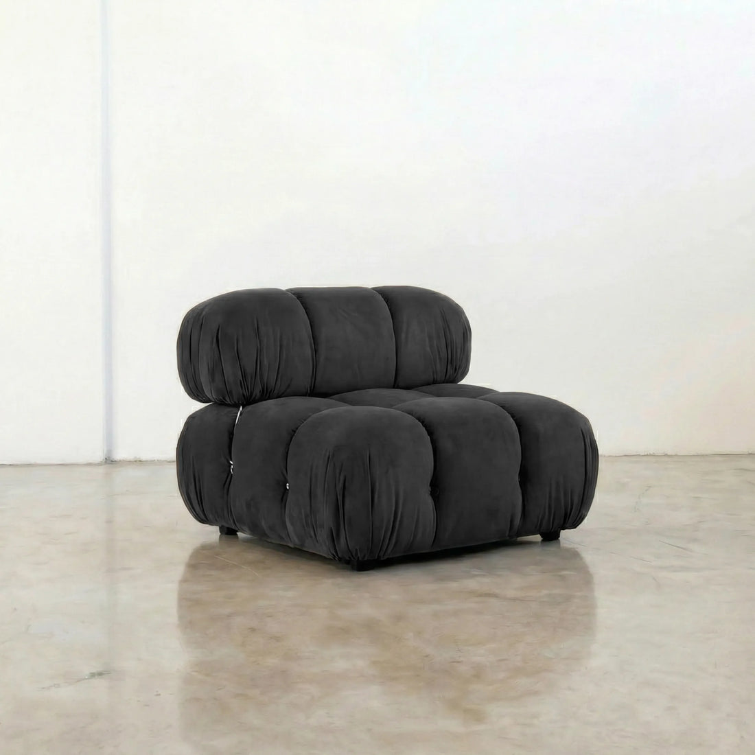 Dark gray camaleonda velvet armless section in a minimalistic room with a white wall and concrete floor.