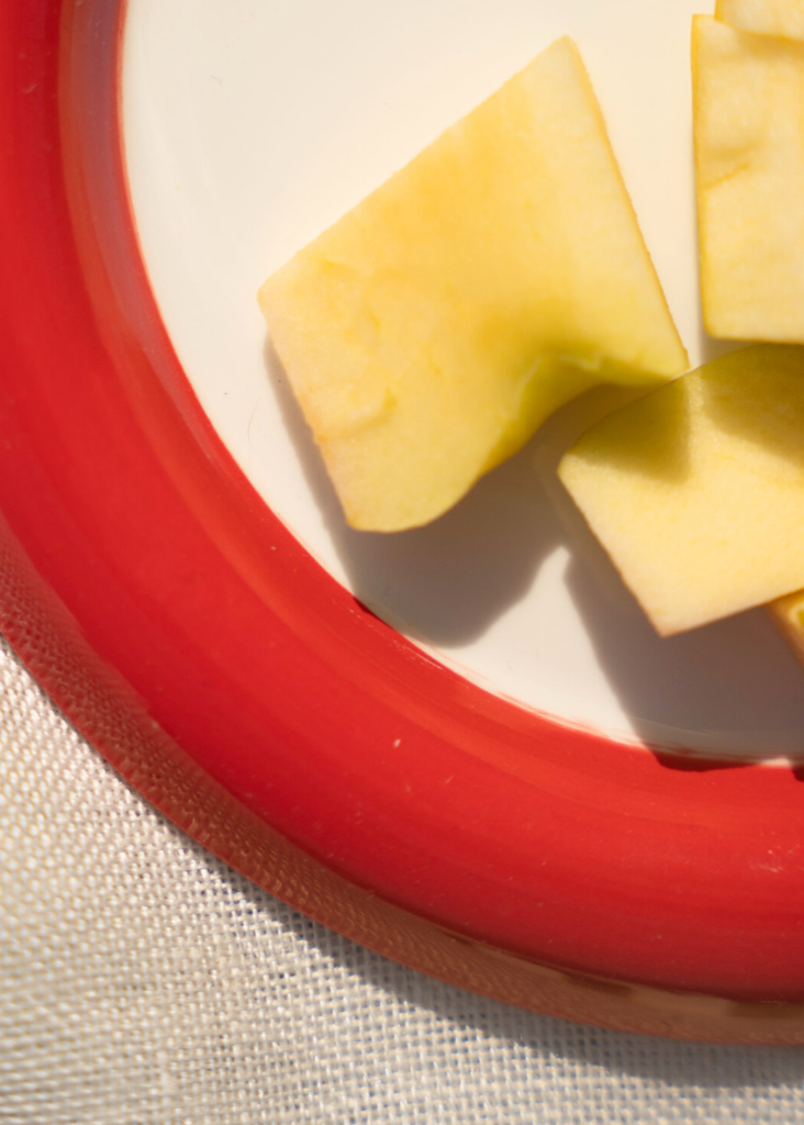 Sliced apples on a red chunky plate with a white background