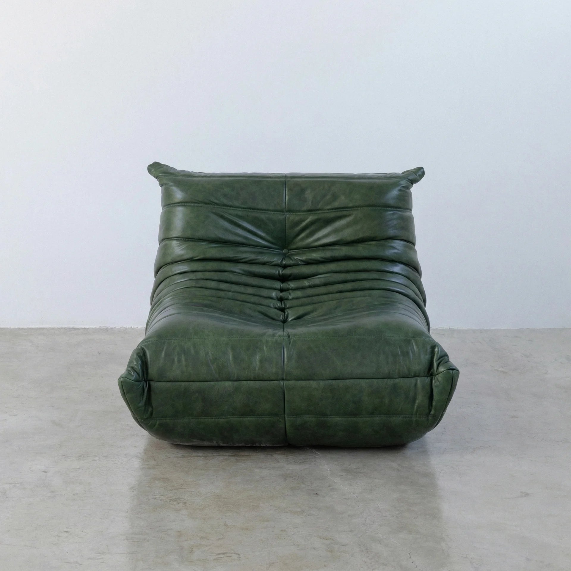 Togo Chair Dupe in green real shiny oil wax leather on a concrete floor with a white wall background
