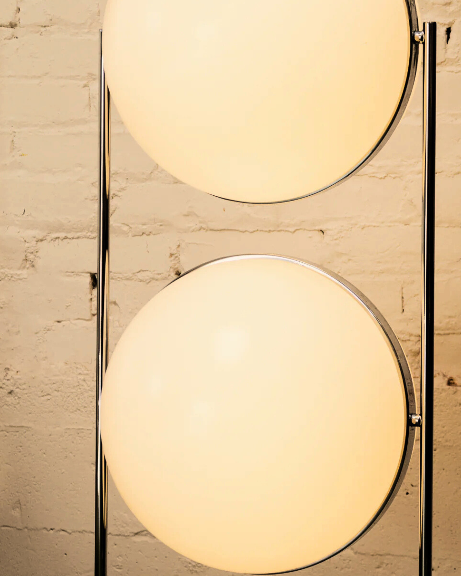 Modern floor globe double lamp with two round glass shades against a brick wall.