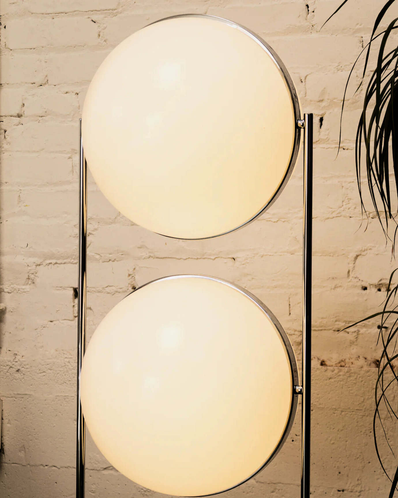 Modern double globe floor lamp with two round glass shades against a brick wall.